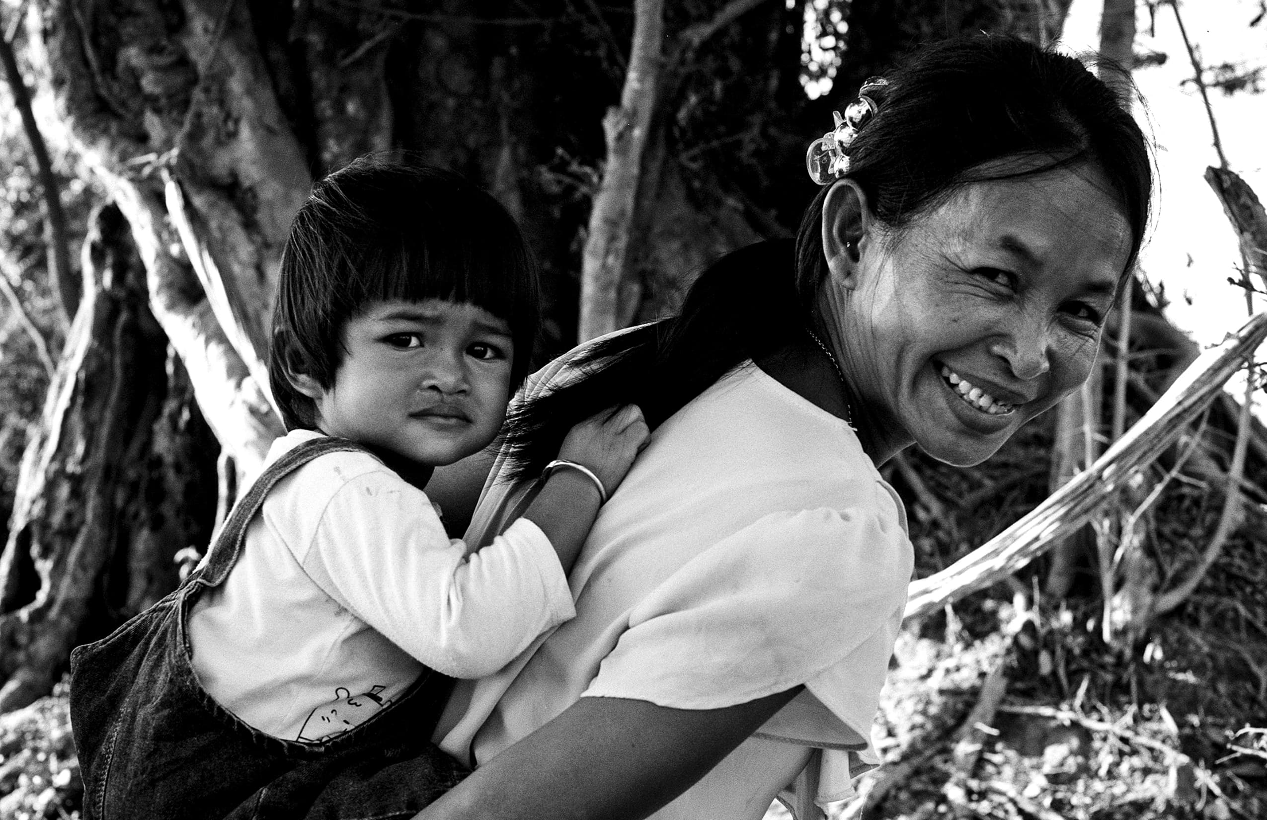 Smiling Cambodian mother carrying young child on her back in natural outdoor setting