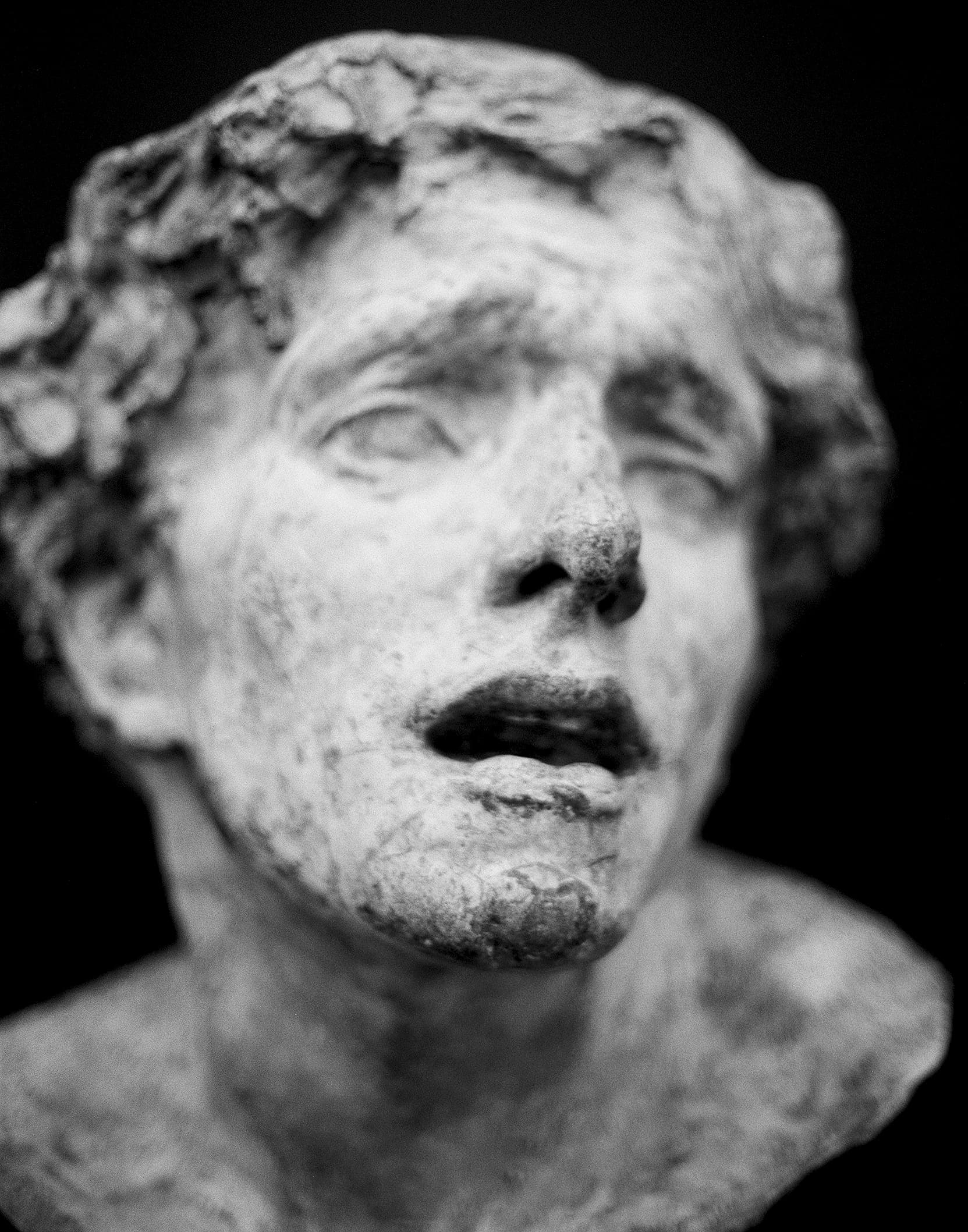 Close-up of weathered classical marble sculpture face with curly hair against dark background
