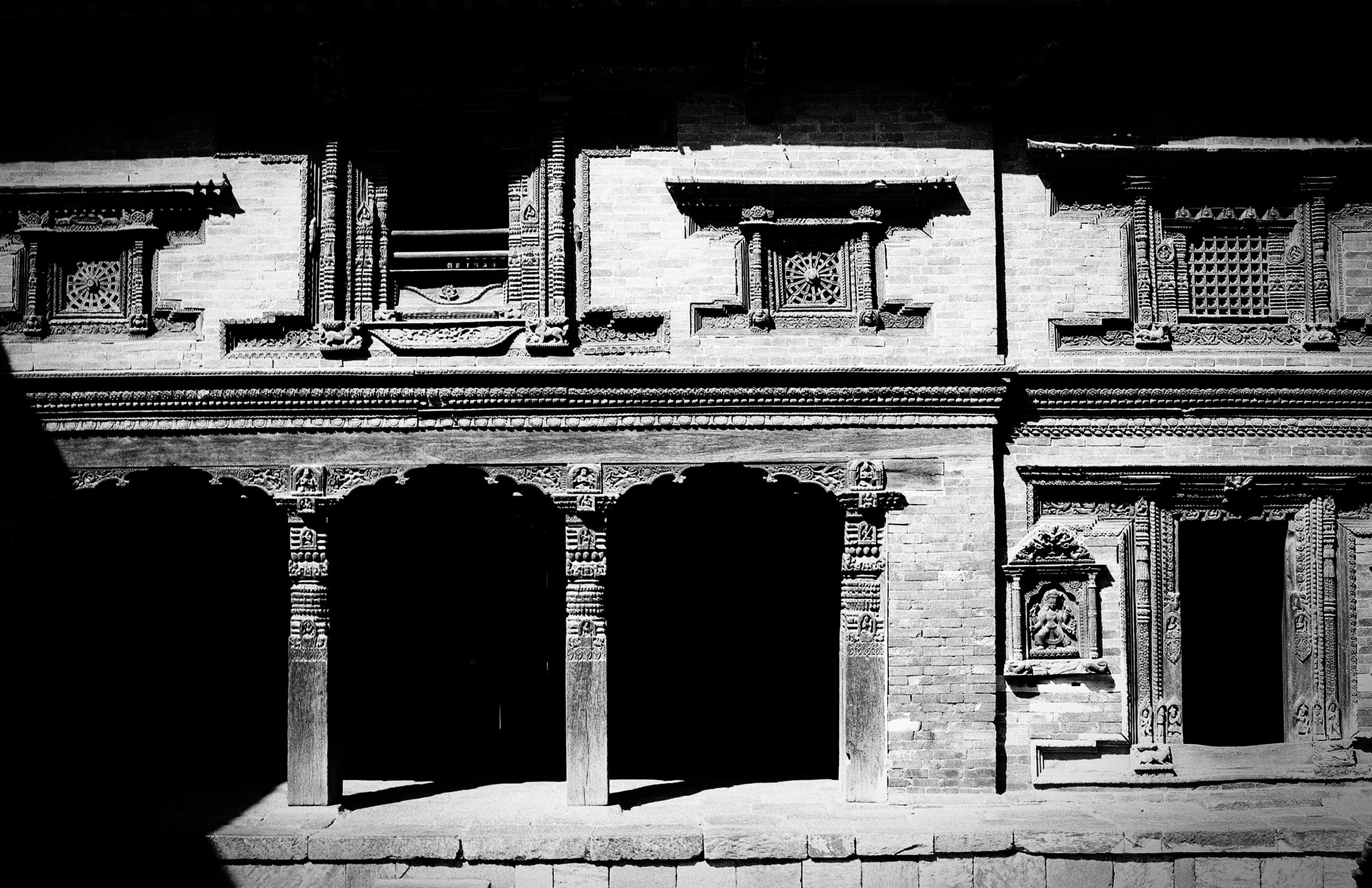 Carved Newari facade with shadowed arches and latticed windows