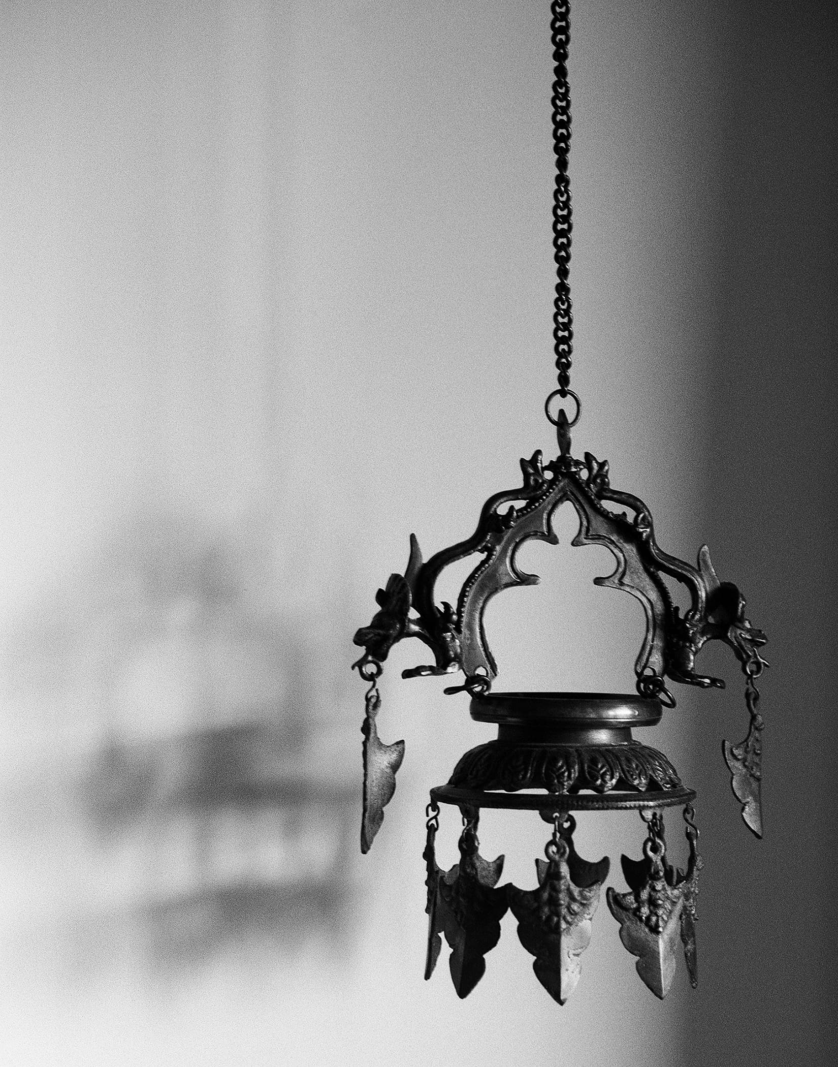 Ornate brass lamp hanging from a chain against a pale wall