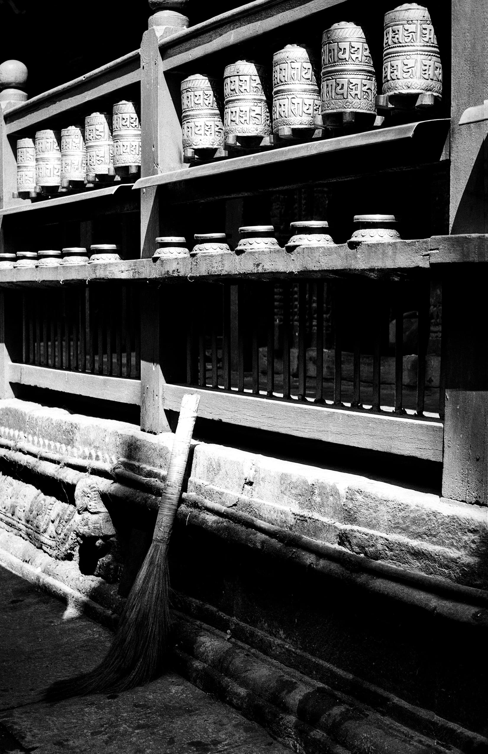 Rows of carved prayer wheels with a broom leaning below