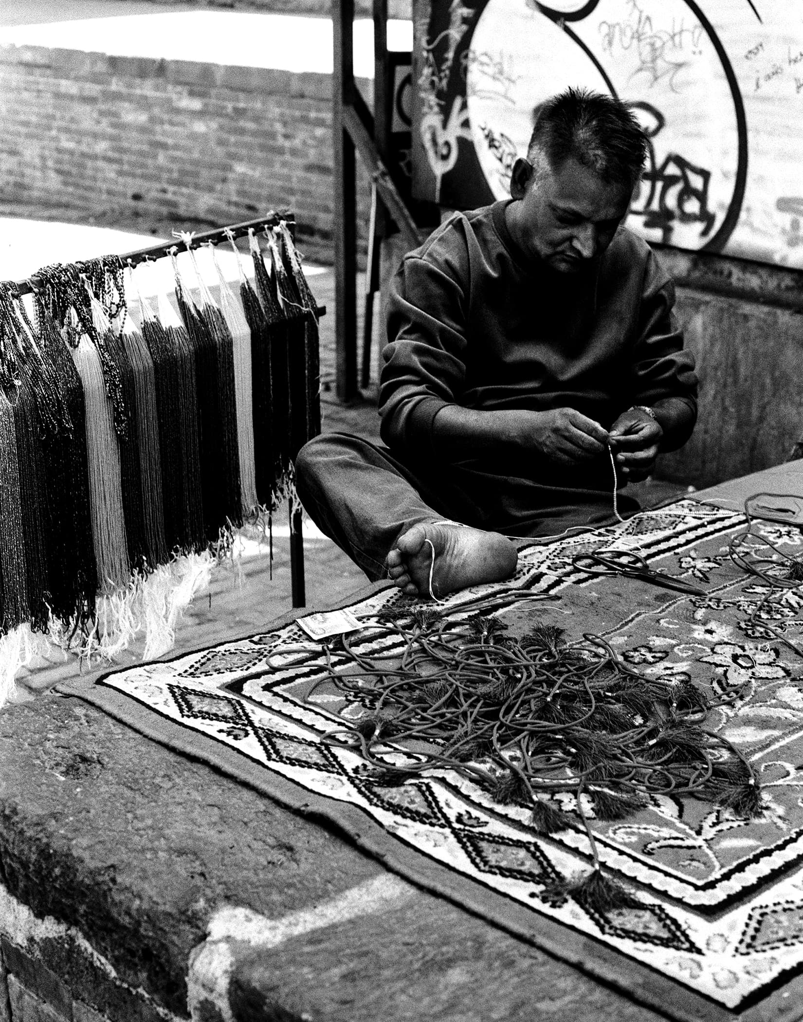 Man stringing beads cross-legged on a patterned rug