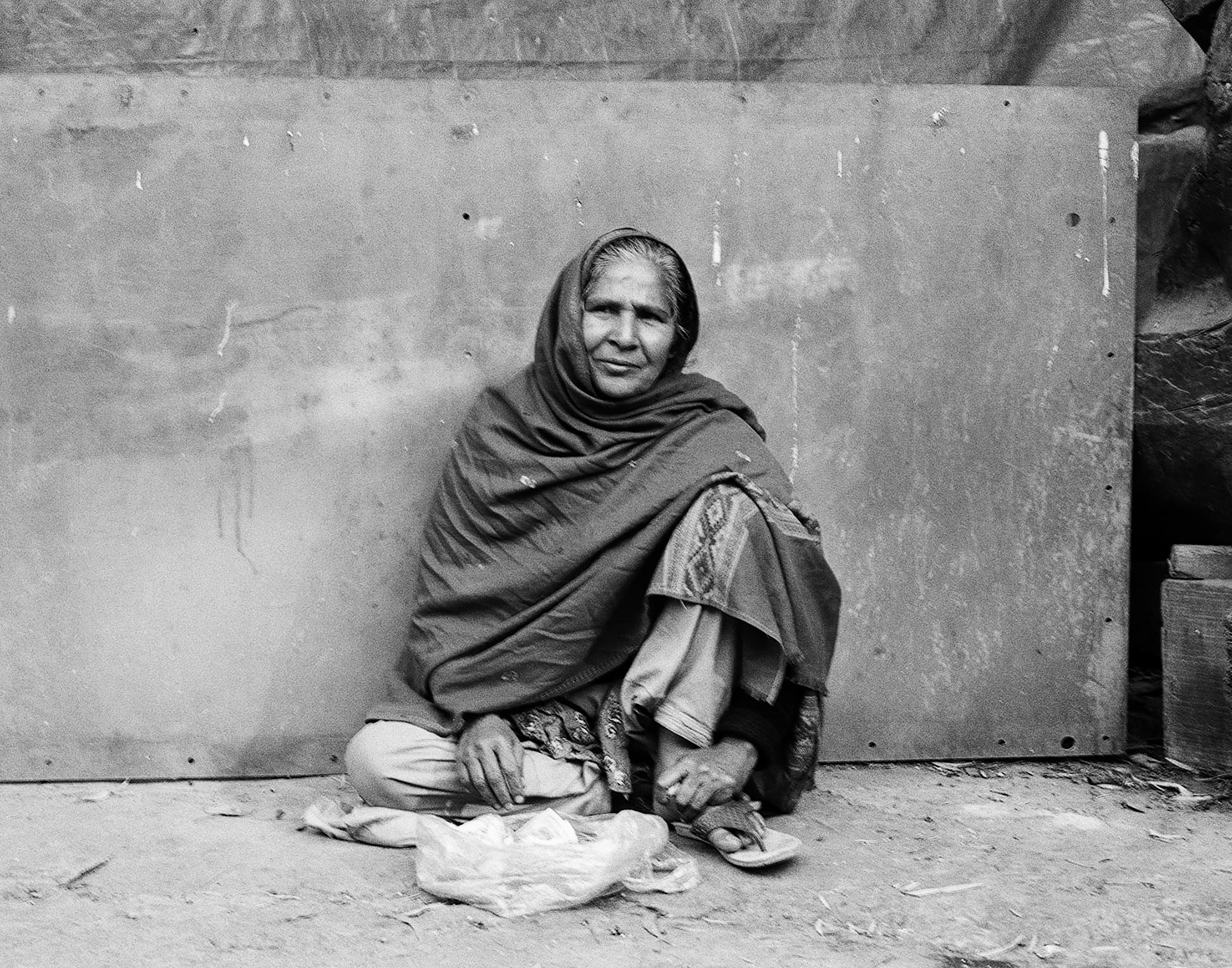 Woman wrapped in a shawl seated against a weathered wall