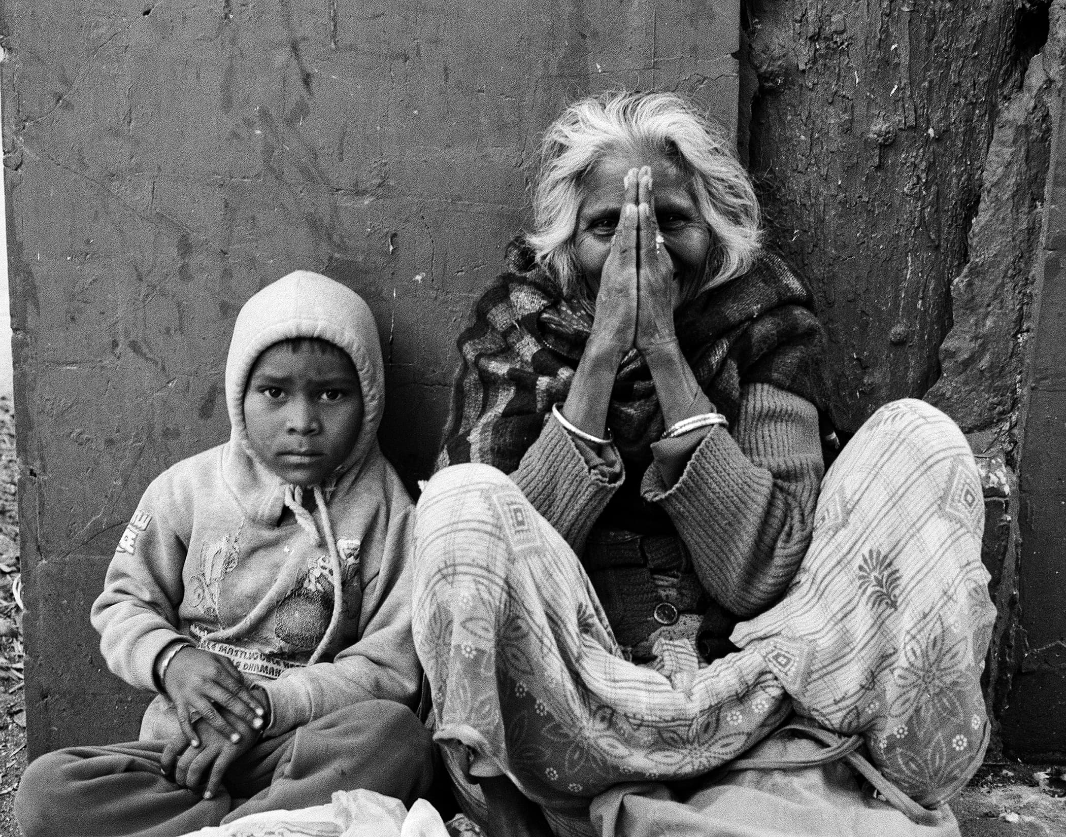 Young boy beside an elderly woman pressing her hands together in greeting