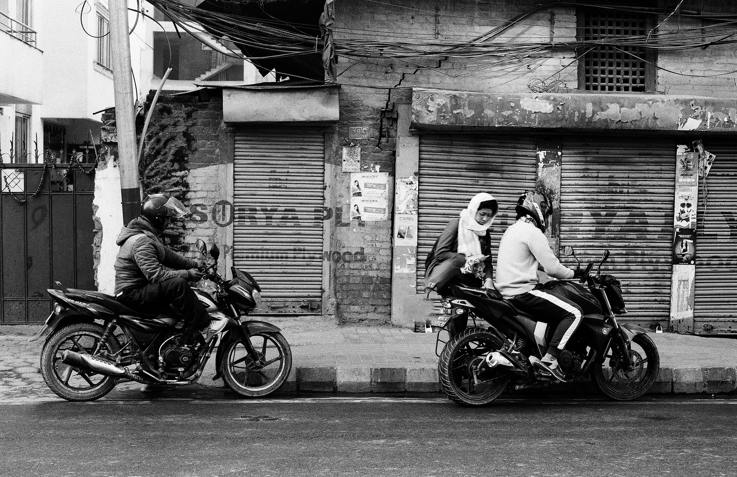Motorcyclists paused in front of shuttered shops beneath tangled wires