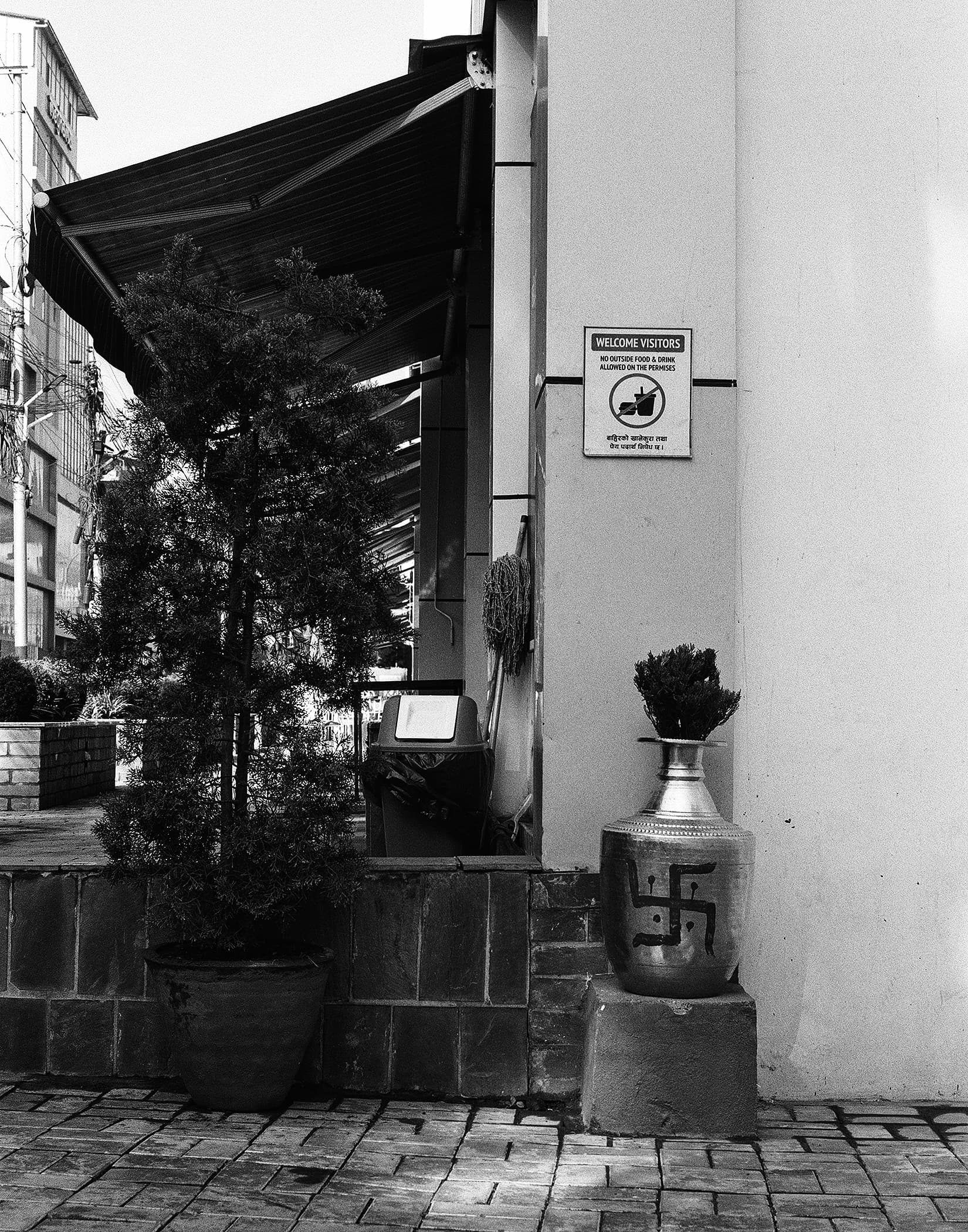 Street corner with awning, potted tree and decorated metal vase