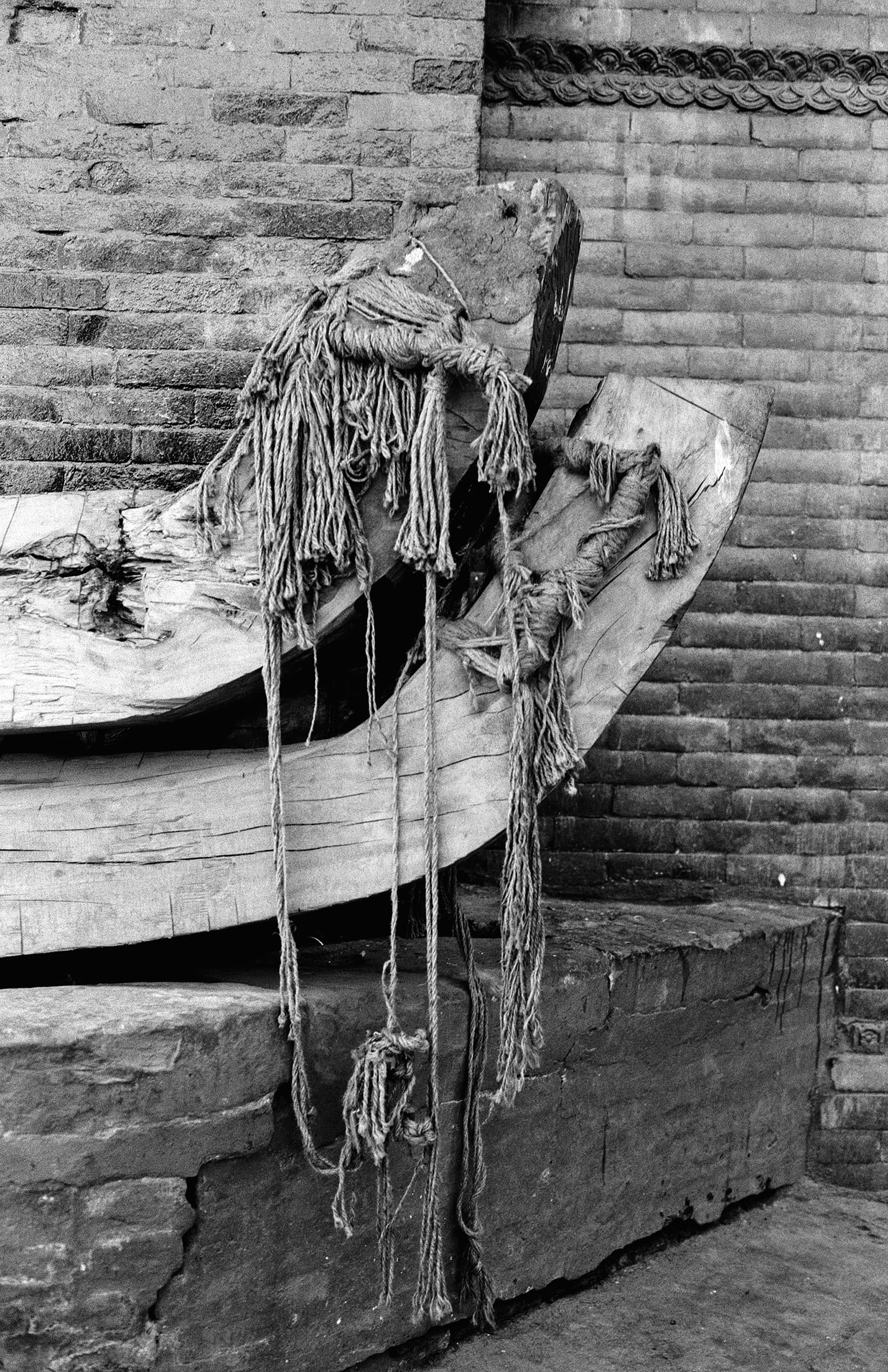 Curved wooden beams bound with frayed rope against brick
