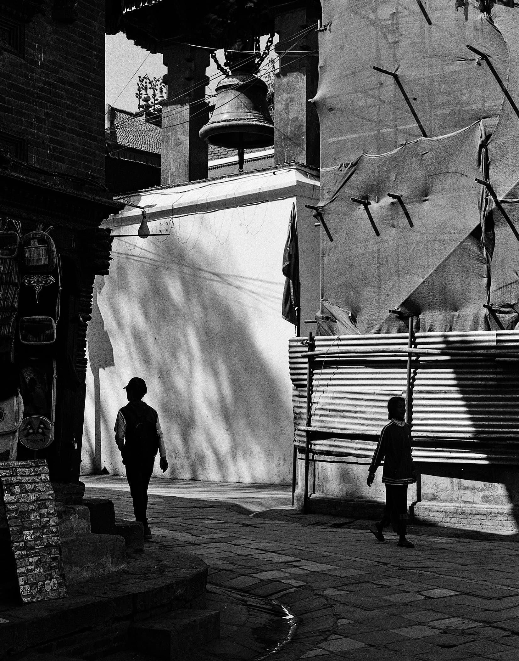 Temple bell above a stone-paved street with two passing figures