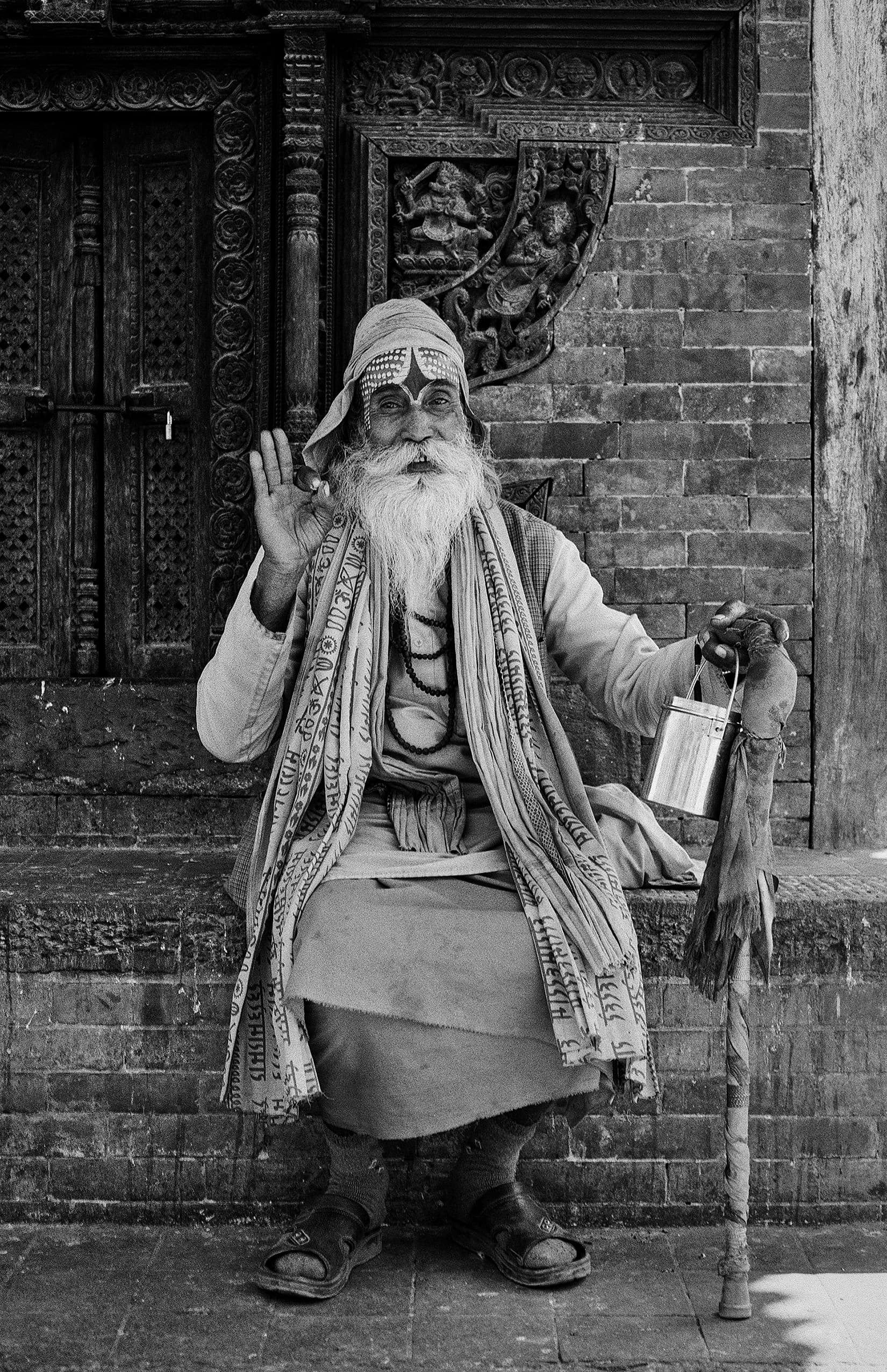 Bearded holy man seated before an ornately carved temple doorway
