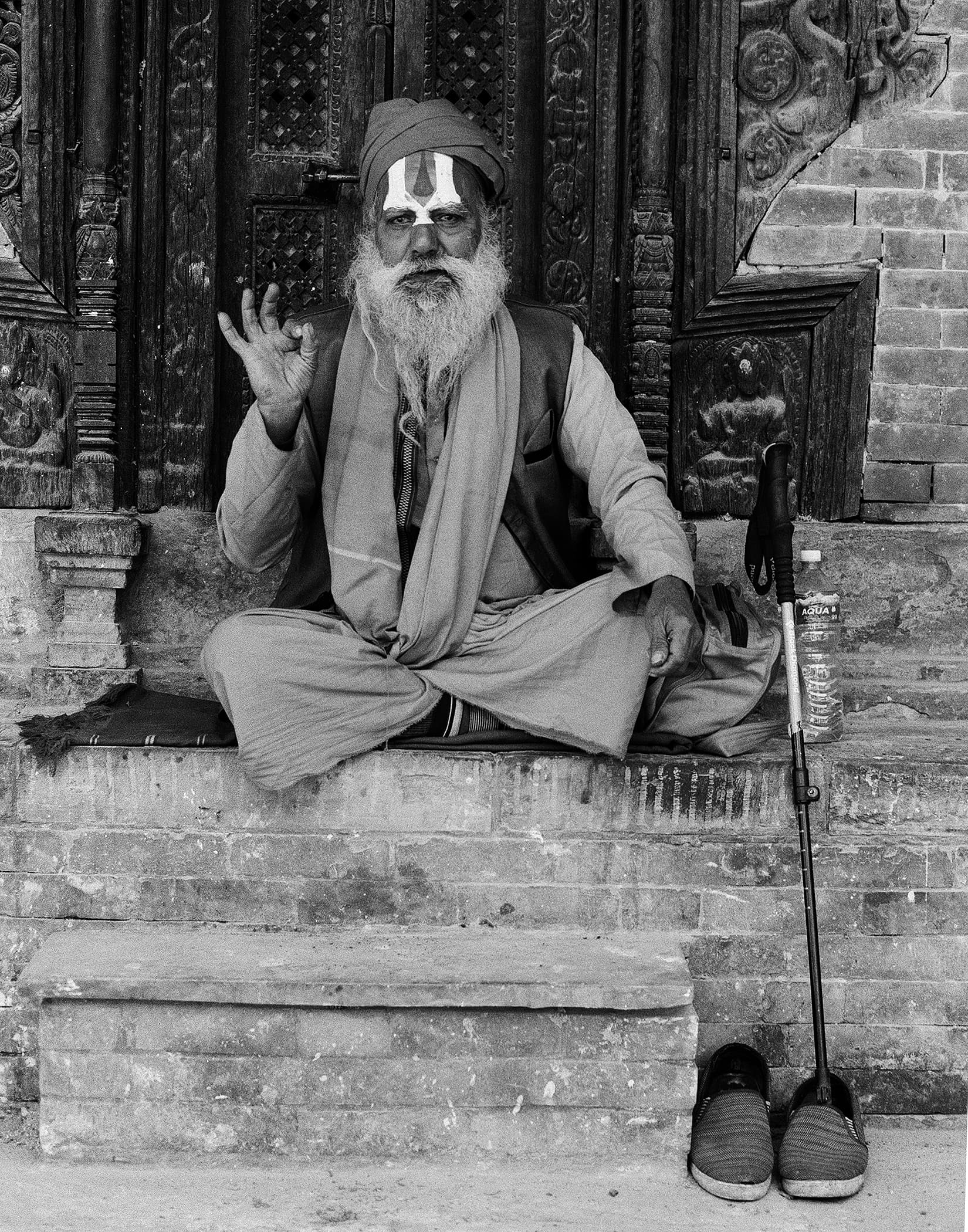 Holy man seated cross-legged with a walking stick and sandals