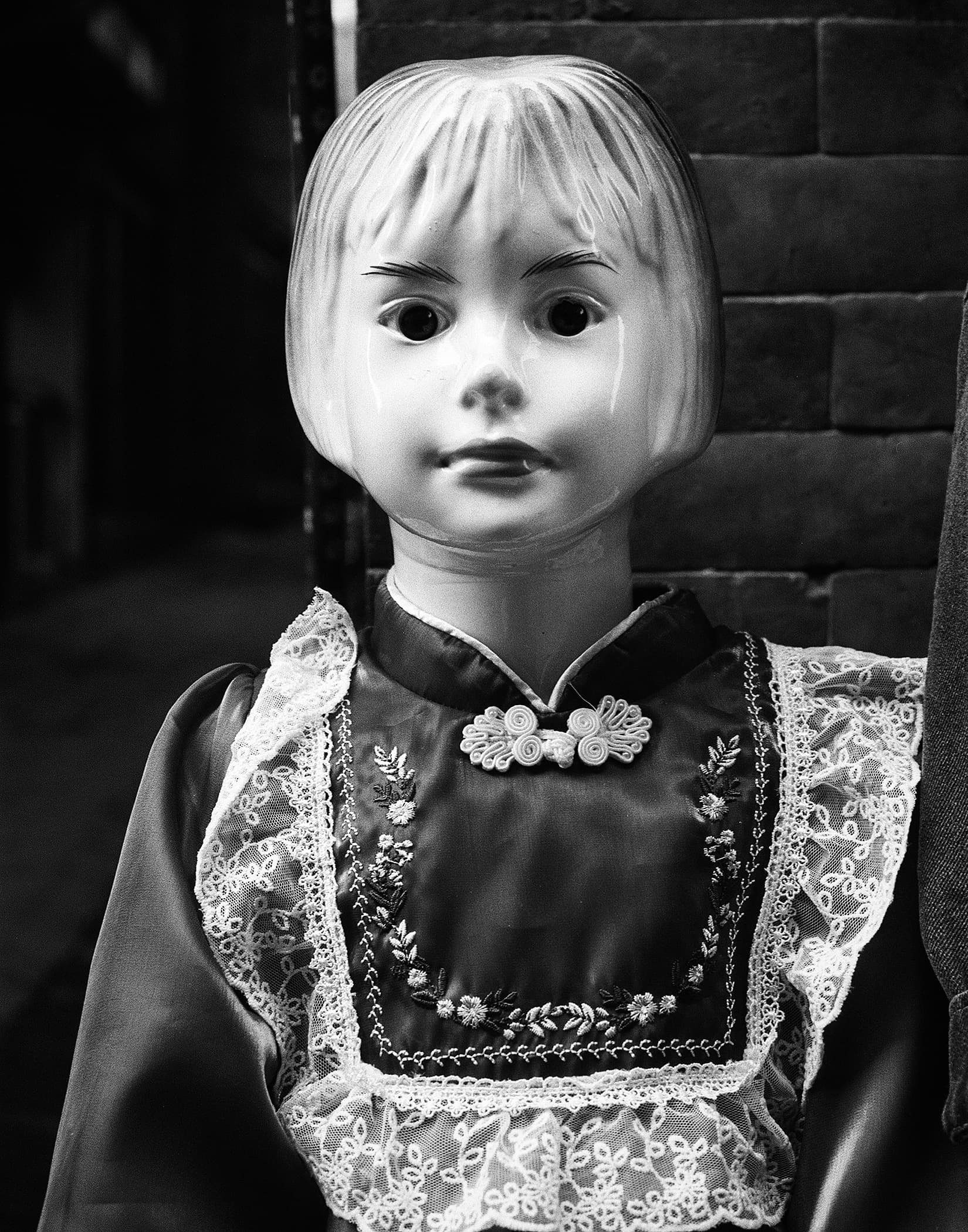 Doll in embroidered clothing displayed against a brick wall