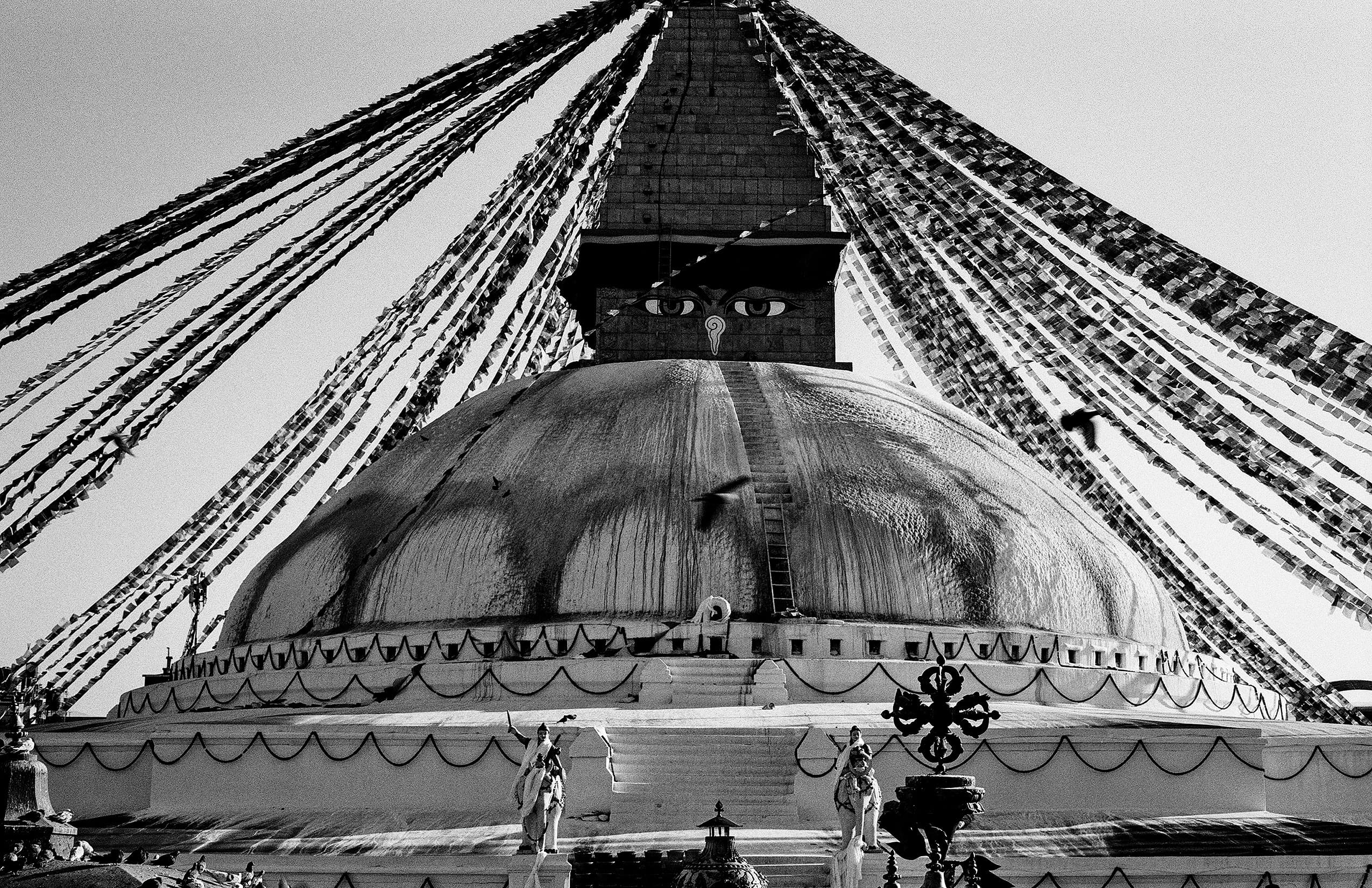 Low-angle view of a stupa dome with prayer flags and devotees