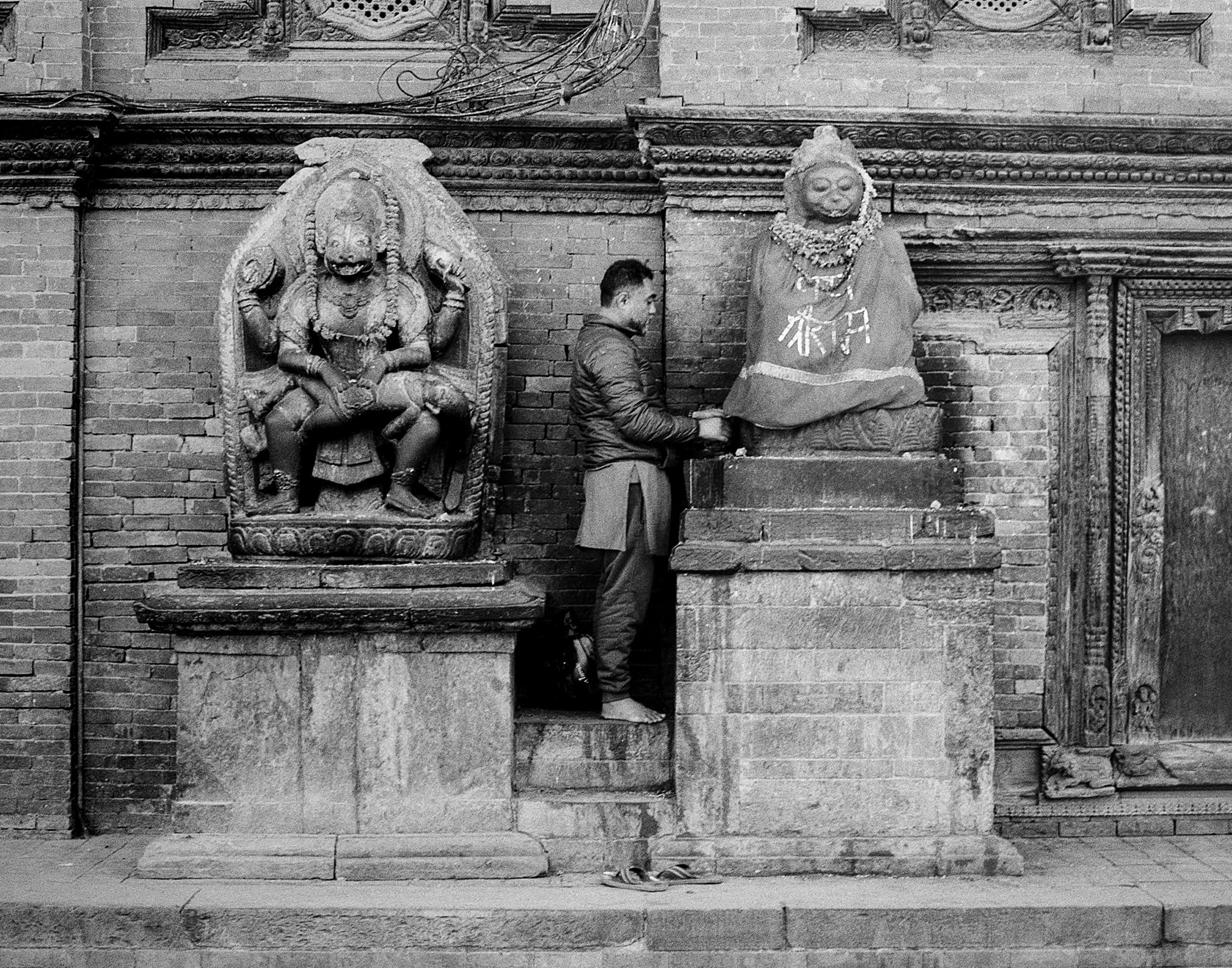 Carved guardian figures and a worshipper beside a temple wall