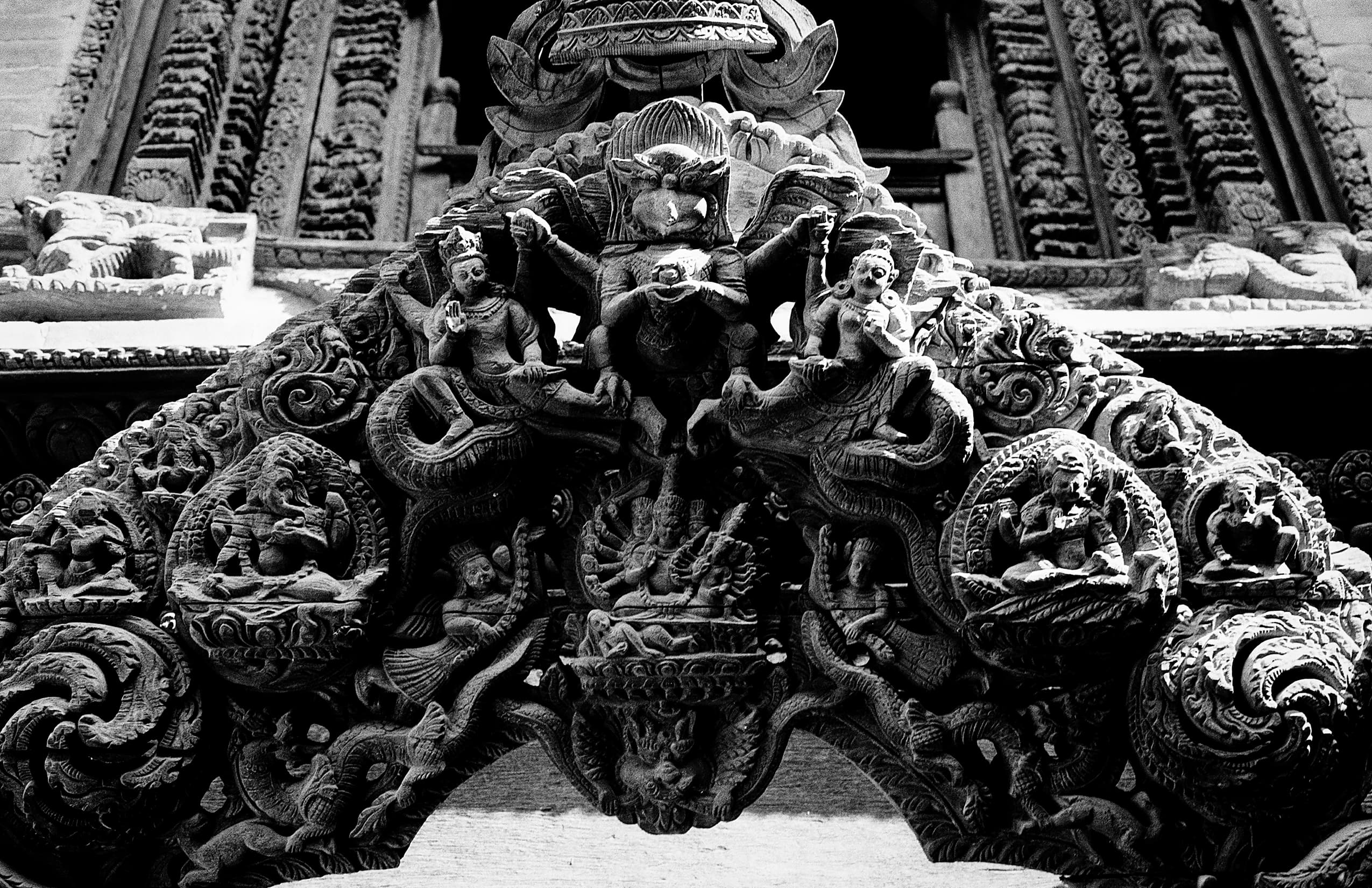 Intricate dark wood carving depicting deities and mythical figures
