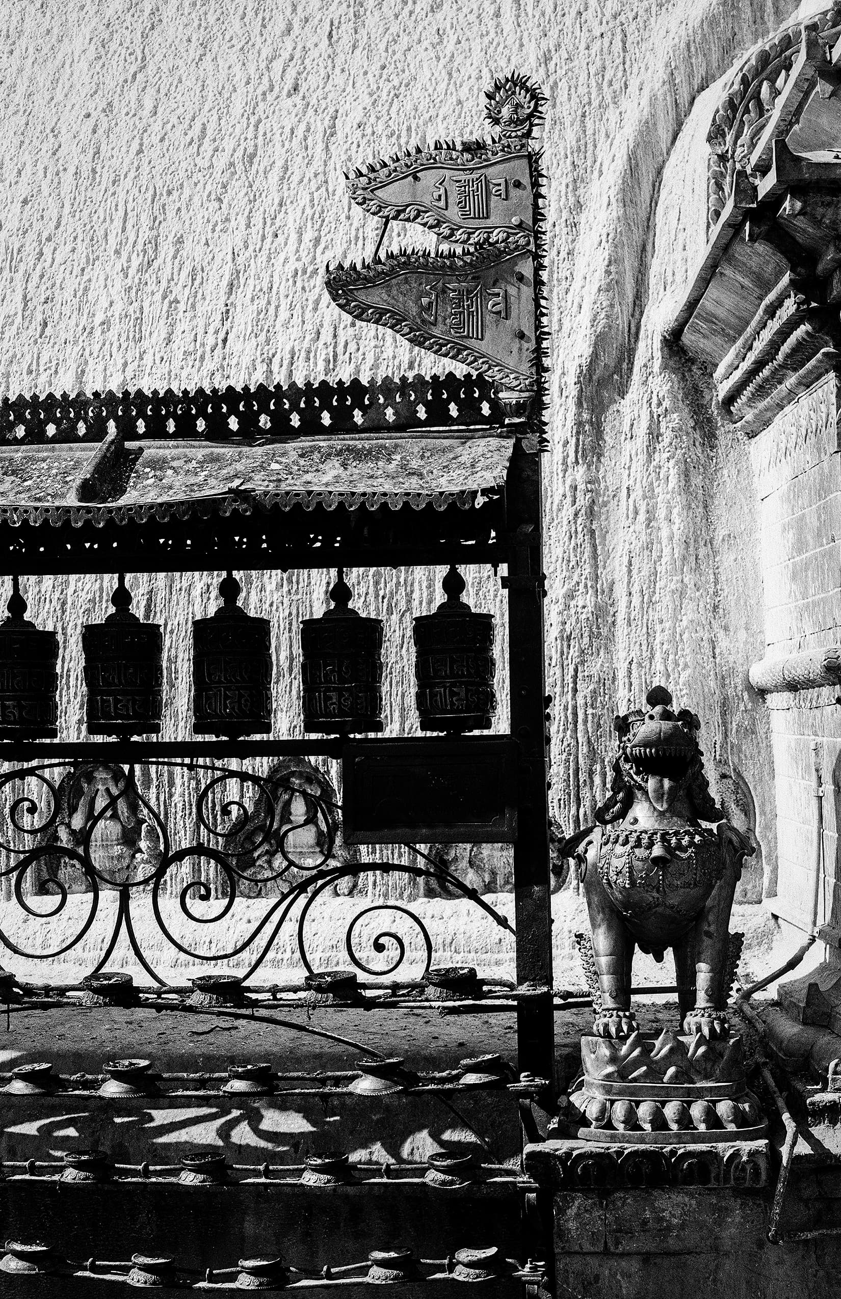 Prayer wheels and a carved guardian figure beside a shrine