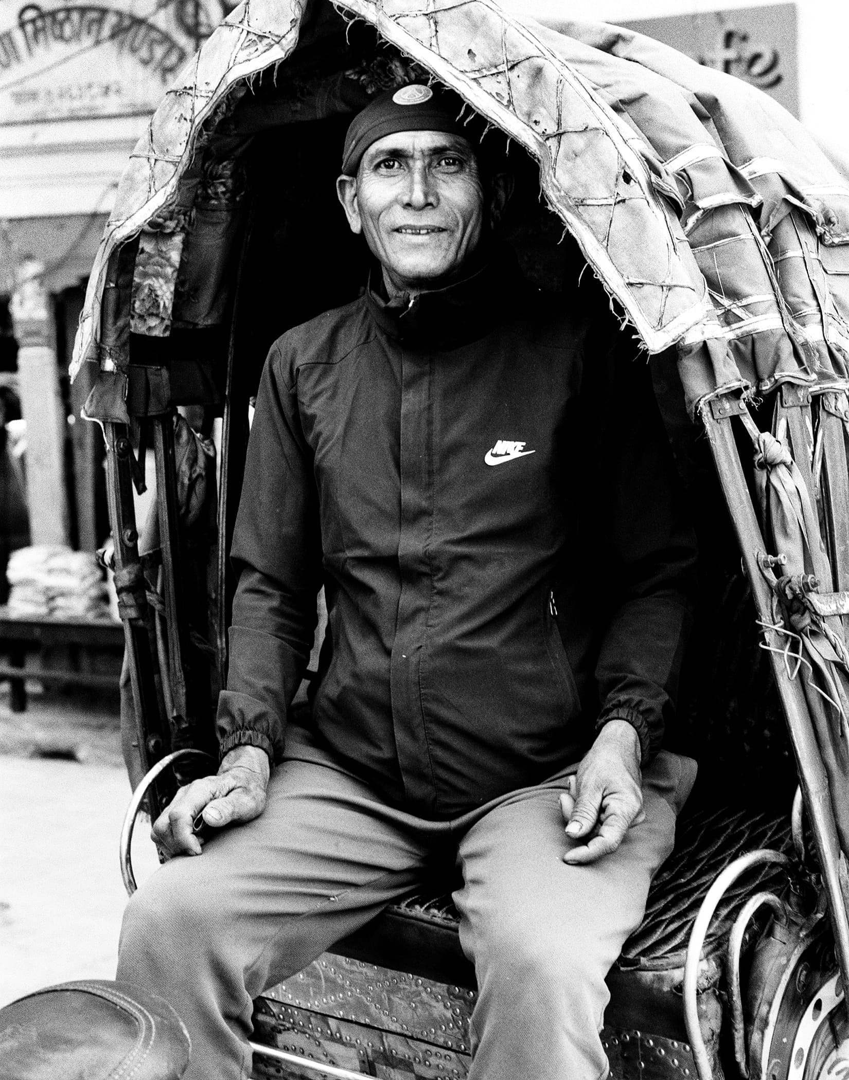 Porter seated beneath a large woven load in a rickshaw