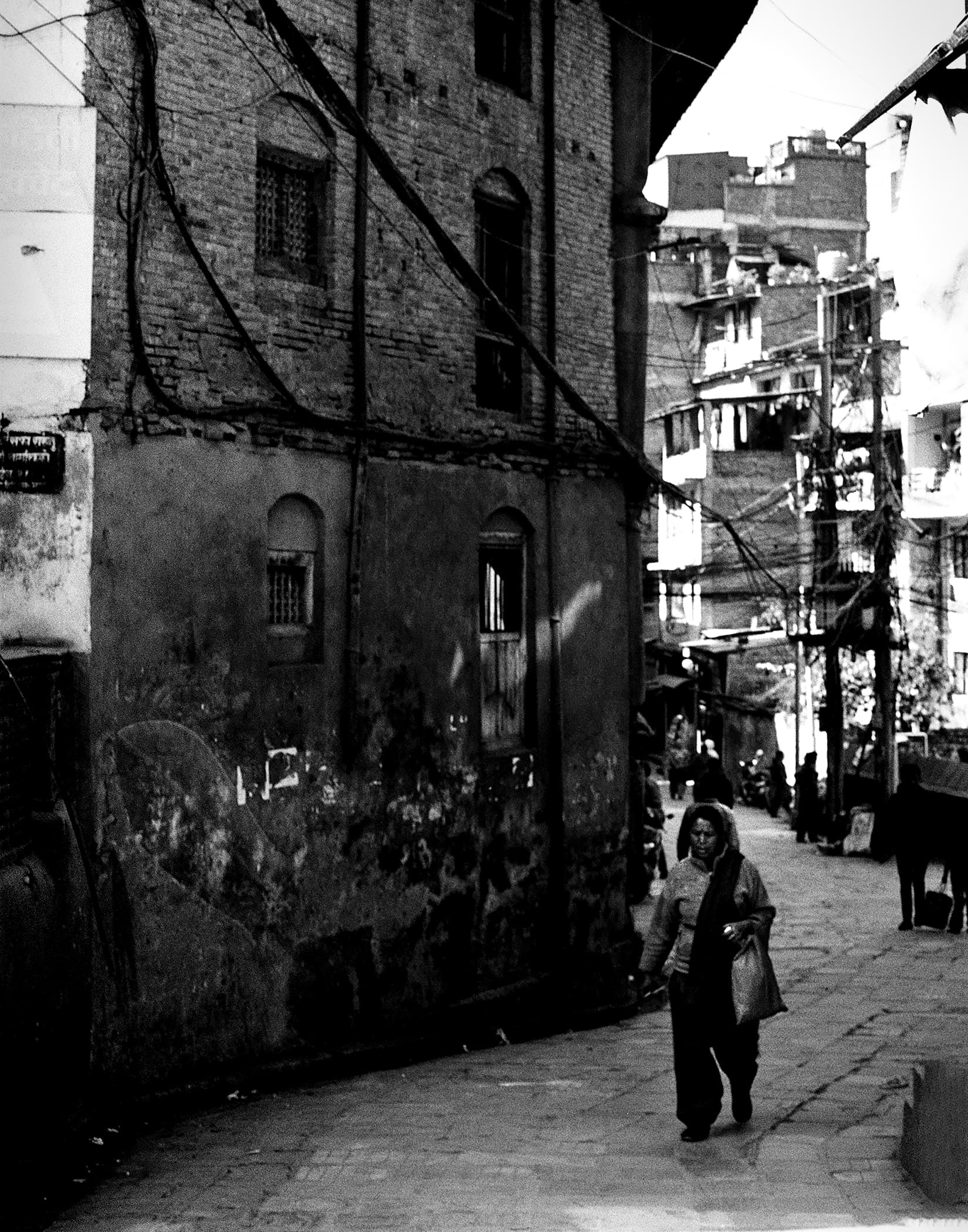 Woman walking through a narrow stone-paved neighborhood lane