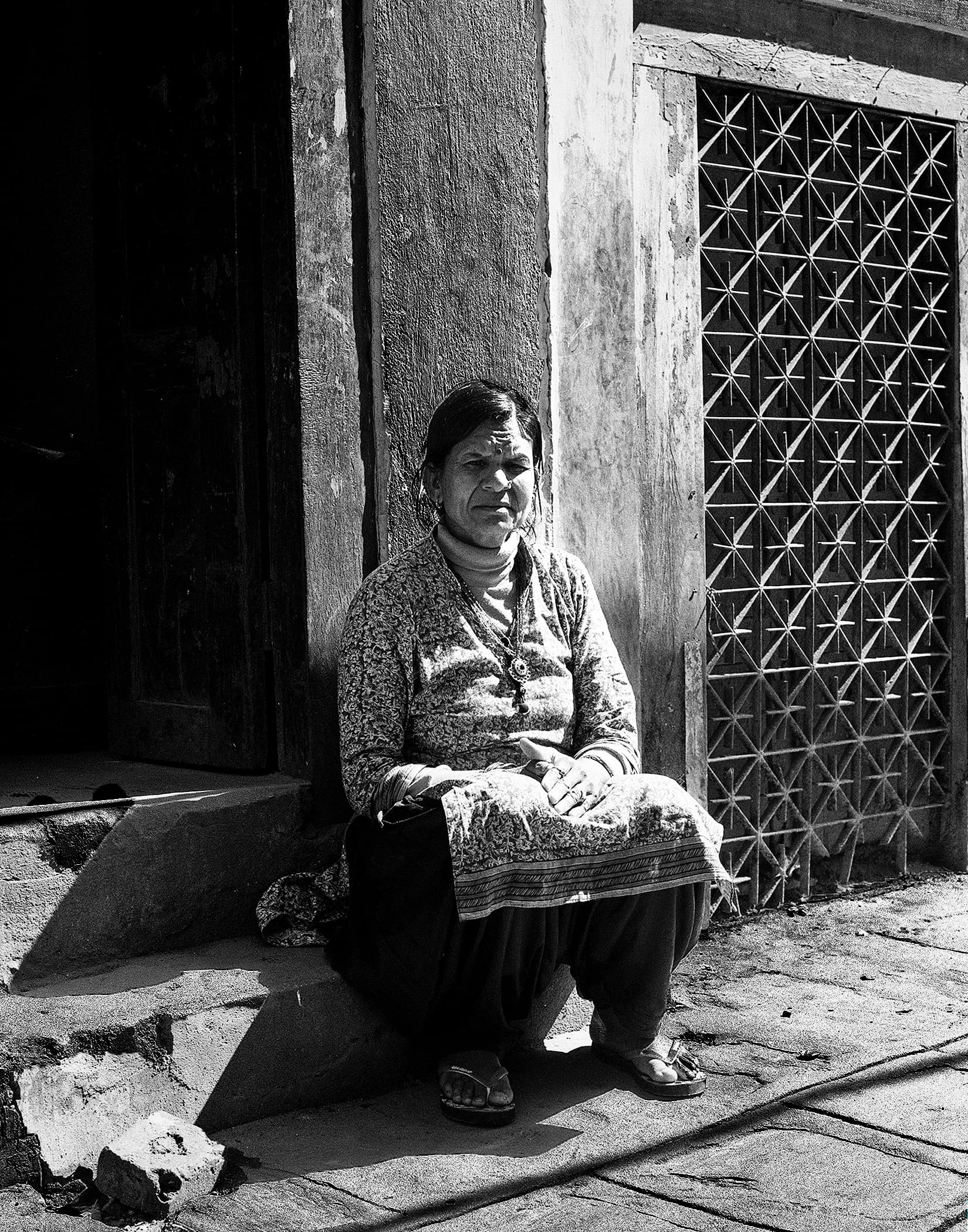 Woman seated in sunlight beside a patterned metal window grille