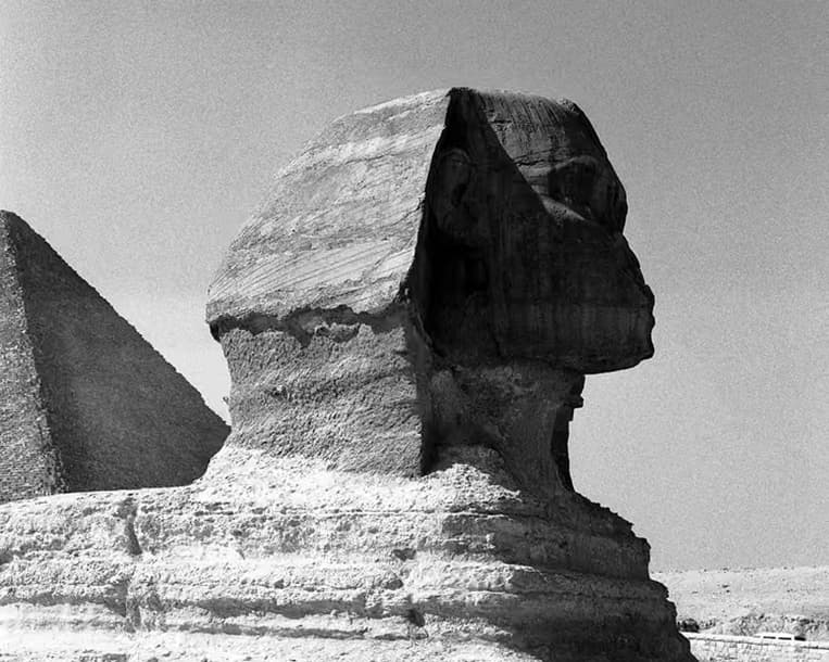 Black-and-white close view of the Great Sphinx with a pyramid behind it