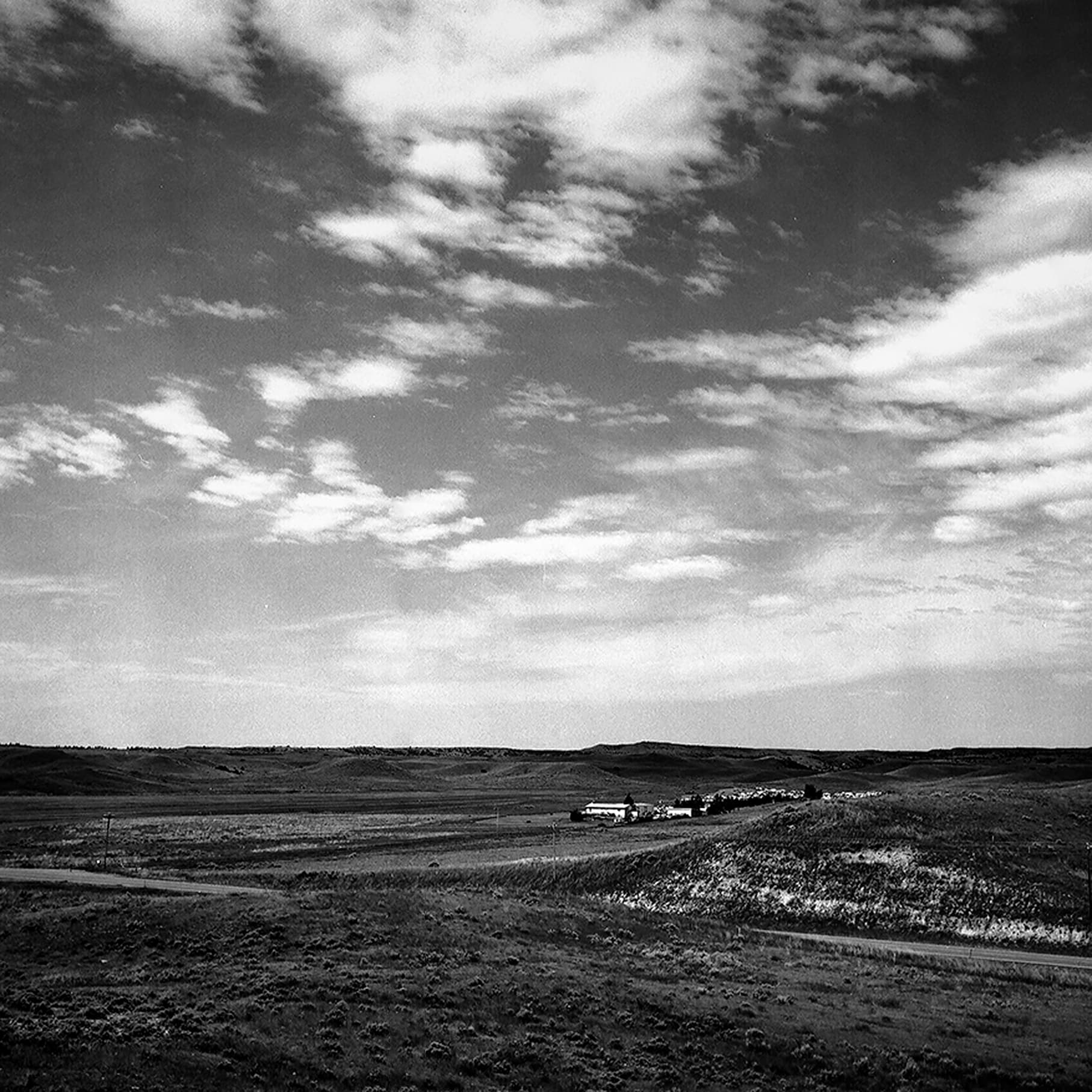 Expansive prairie landscape with dramatic big sky clouds and isolated farm buildings in rolling hills distance