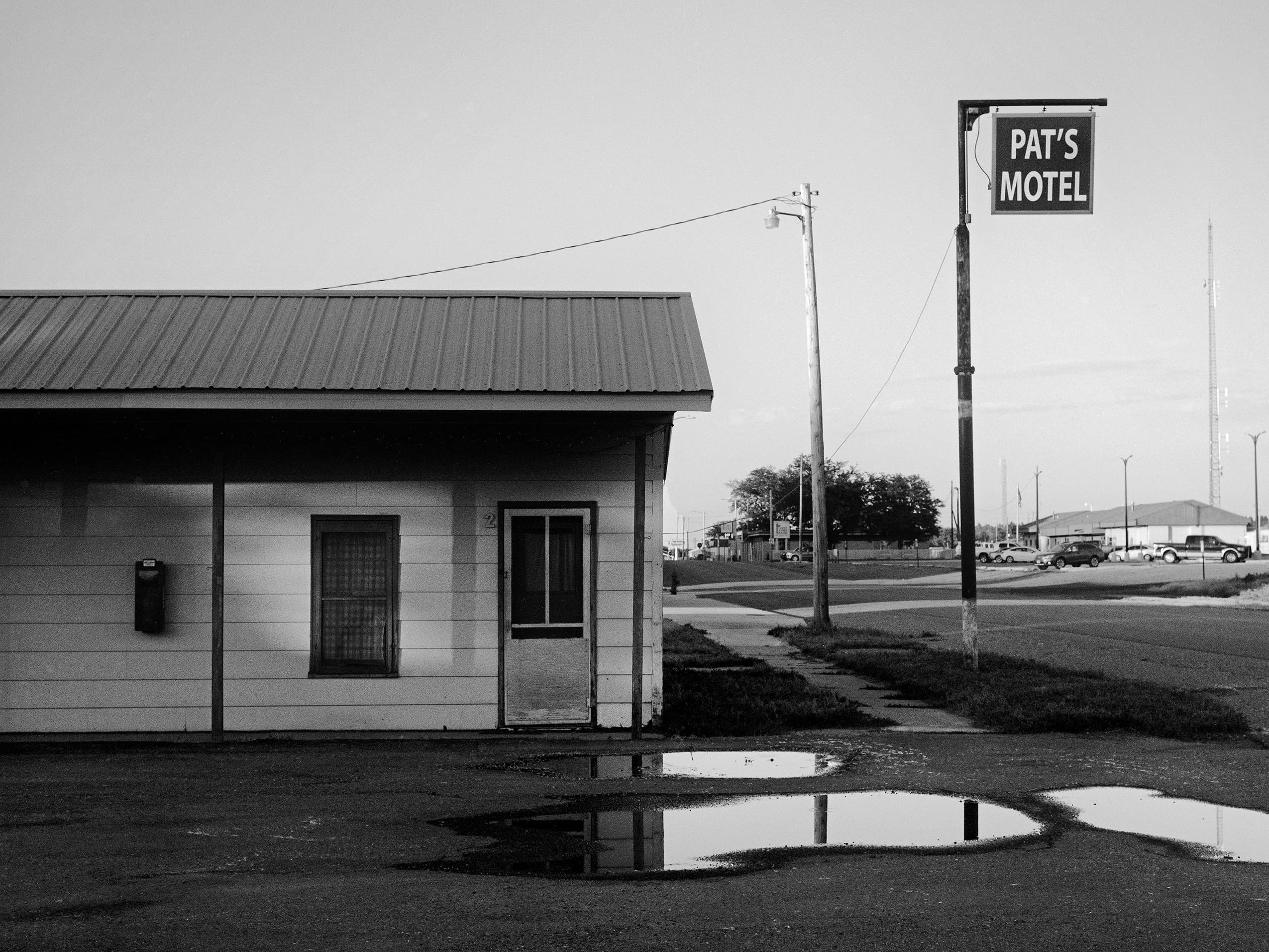 Pat's Motel with vintage sign and puddles reflecting in empty parking lot under overcast sky