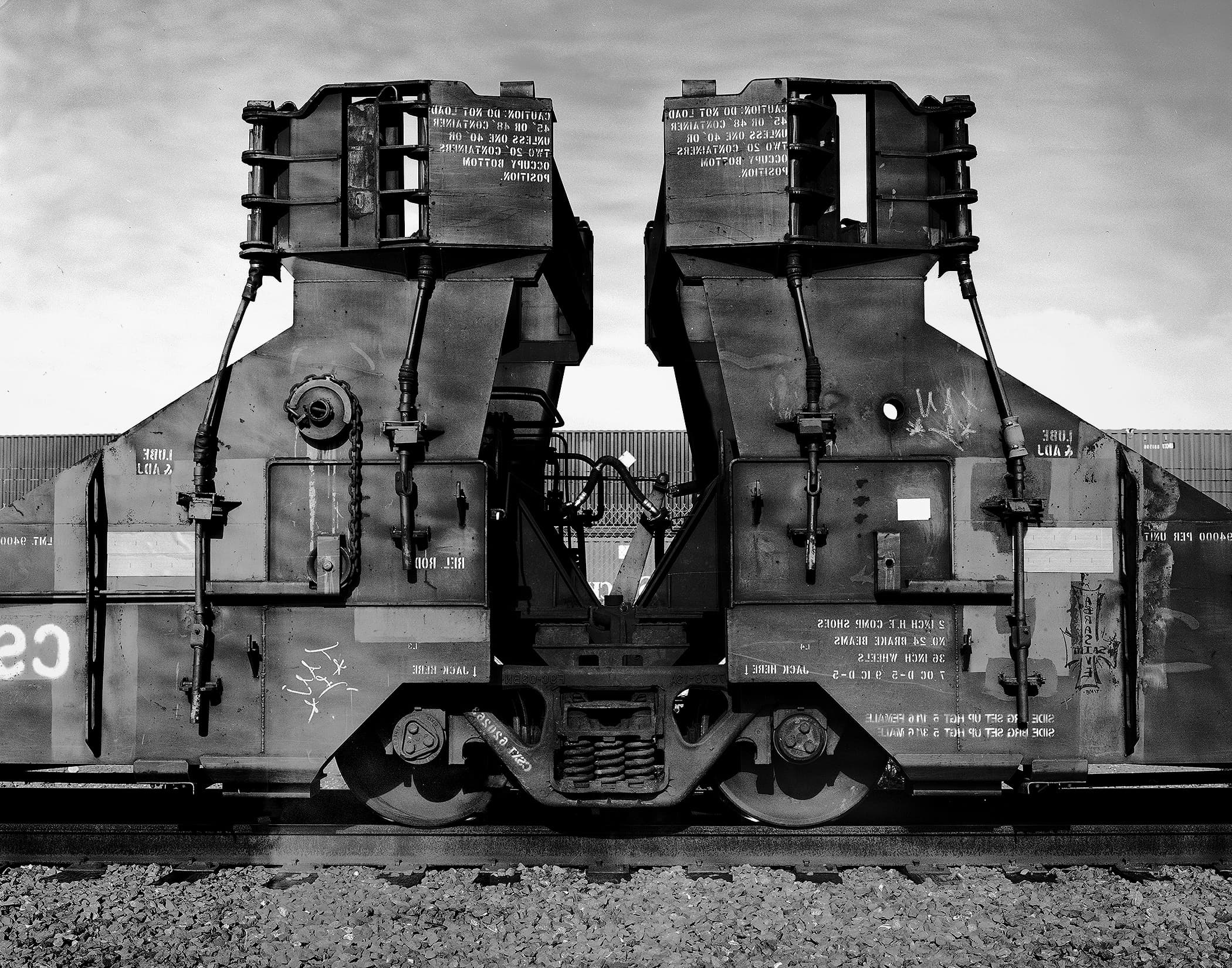 Black-and-white frontal view of a freight railcar with heavy industrial machinery and tracks