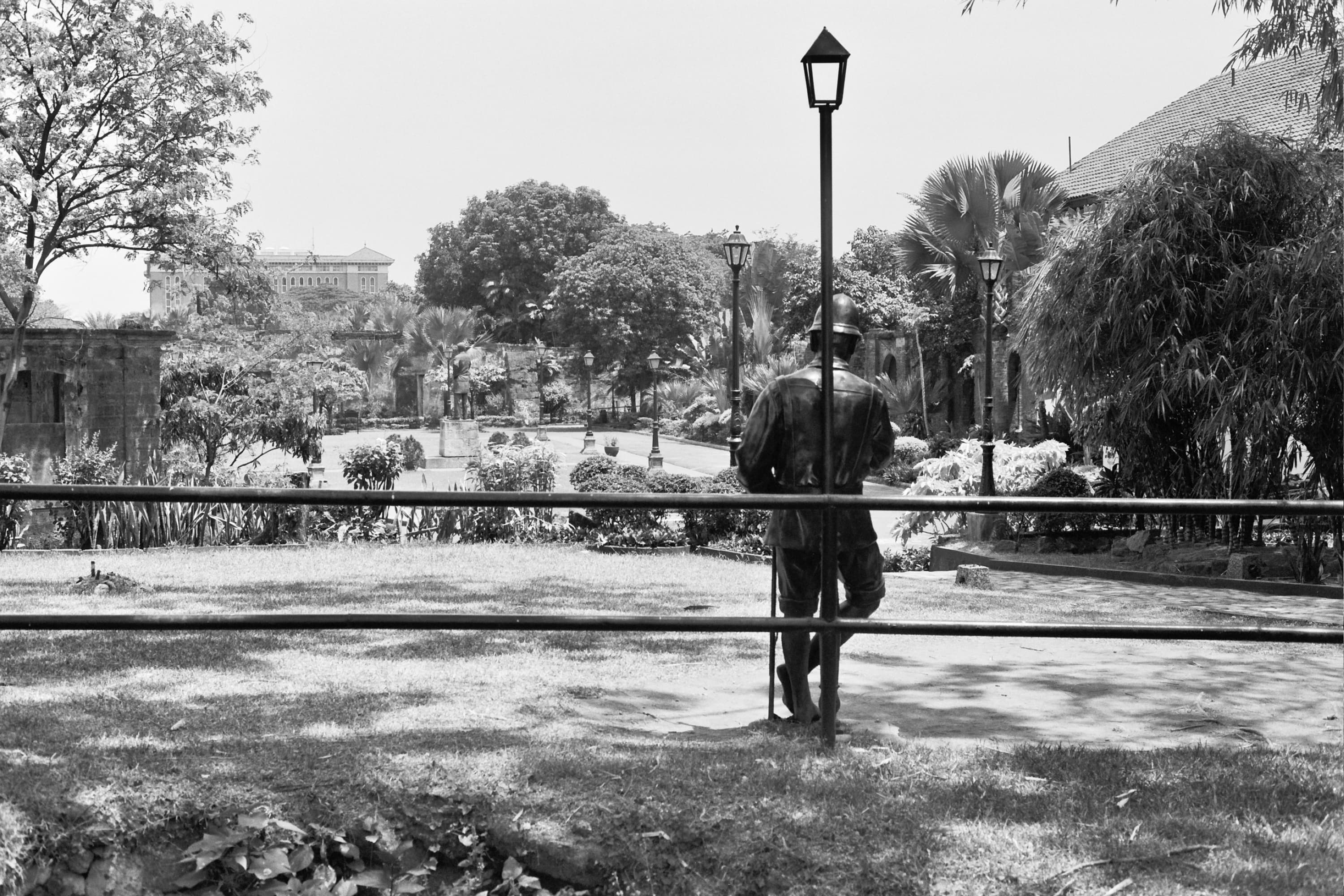 Bronze soldier statue leaning on a lamppost behind a railing in the gardens of Fort Santiago