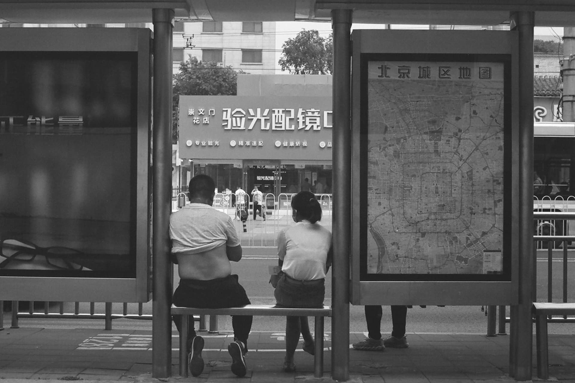 Bus stop shelter with two people viewing map and architectural glass panels reflecting surroundings