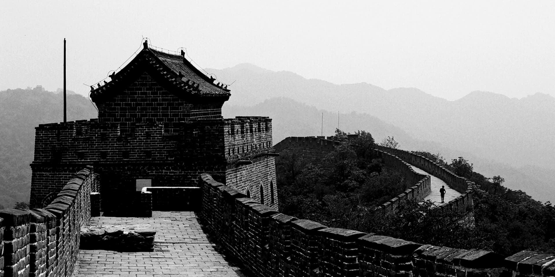 Great Wall section with watchtower and fortification rising through misty forested mountains