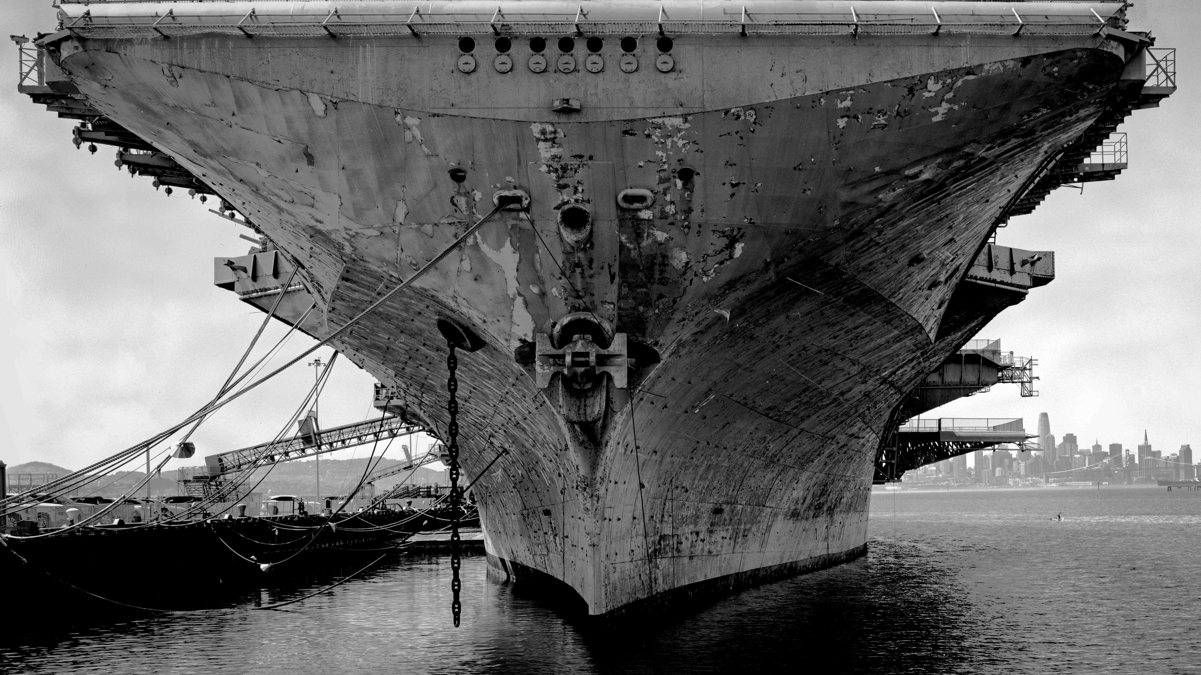 Weathered aircraft carrier bow in the harbor with cranes and the San Francisco skyline in the distance