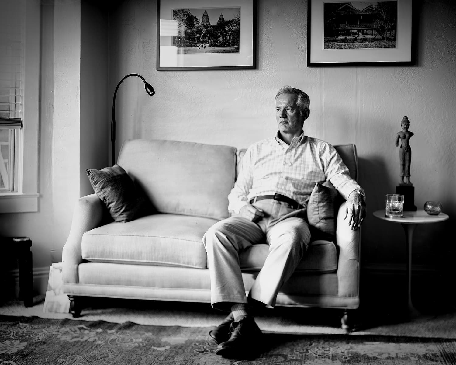 Seated man in a quiet living room beneath framed photographs