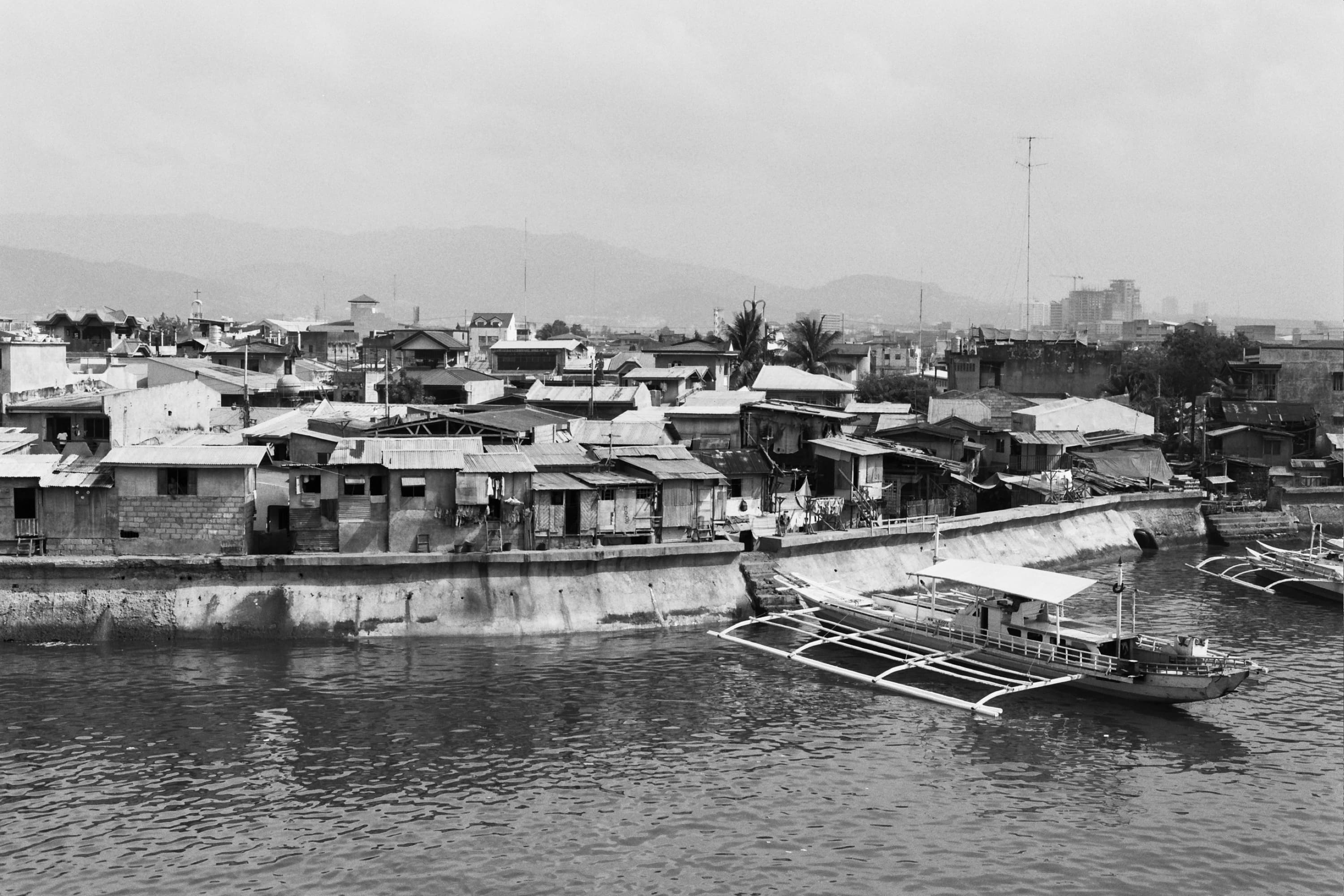 Waterfront shanties along a sea wall with an outrigger bangka moored in the harbor