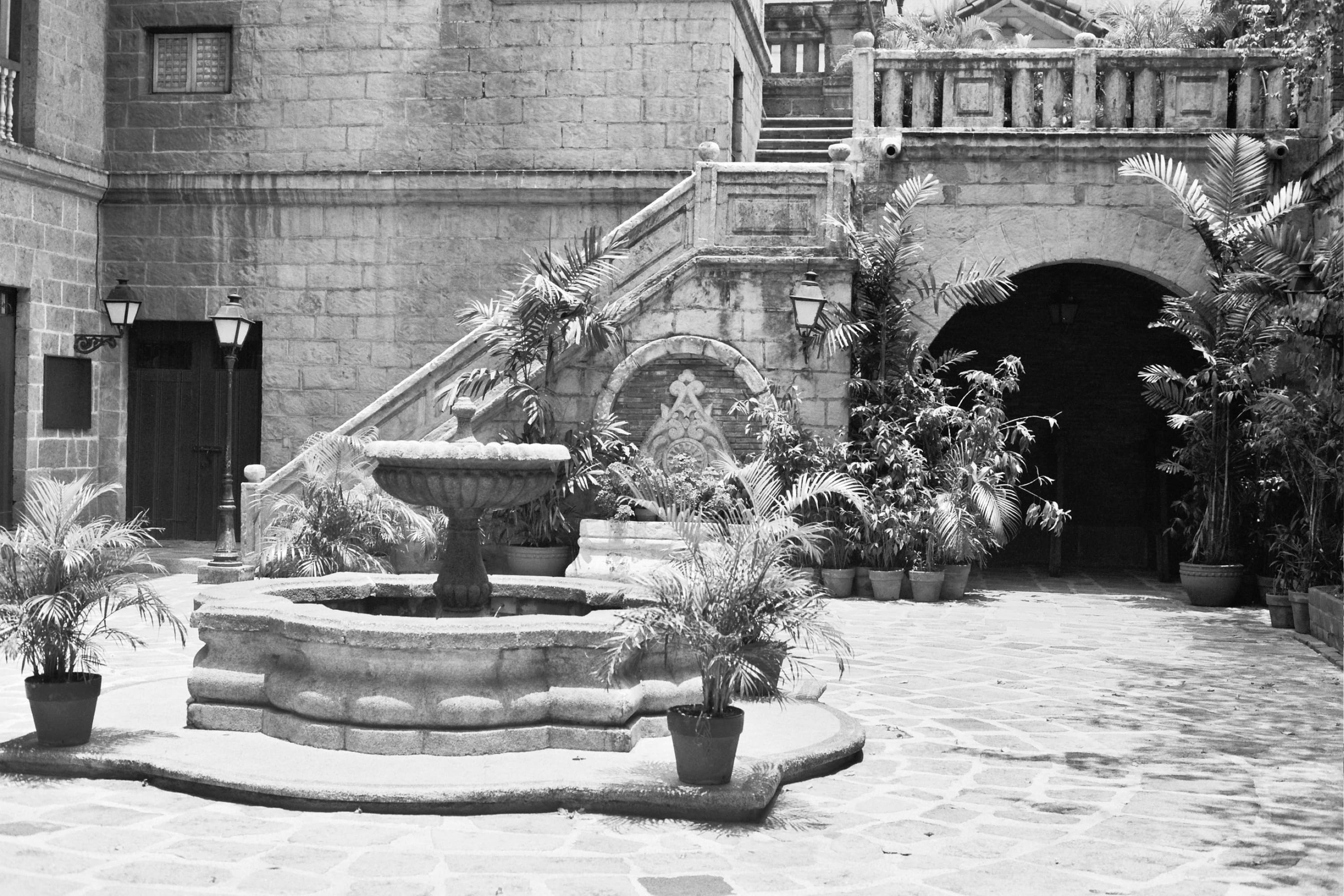 Spanish colonial courtyard with stone fountain, potted palms and grand staircase in Intramuros