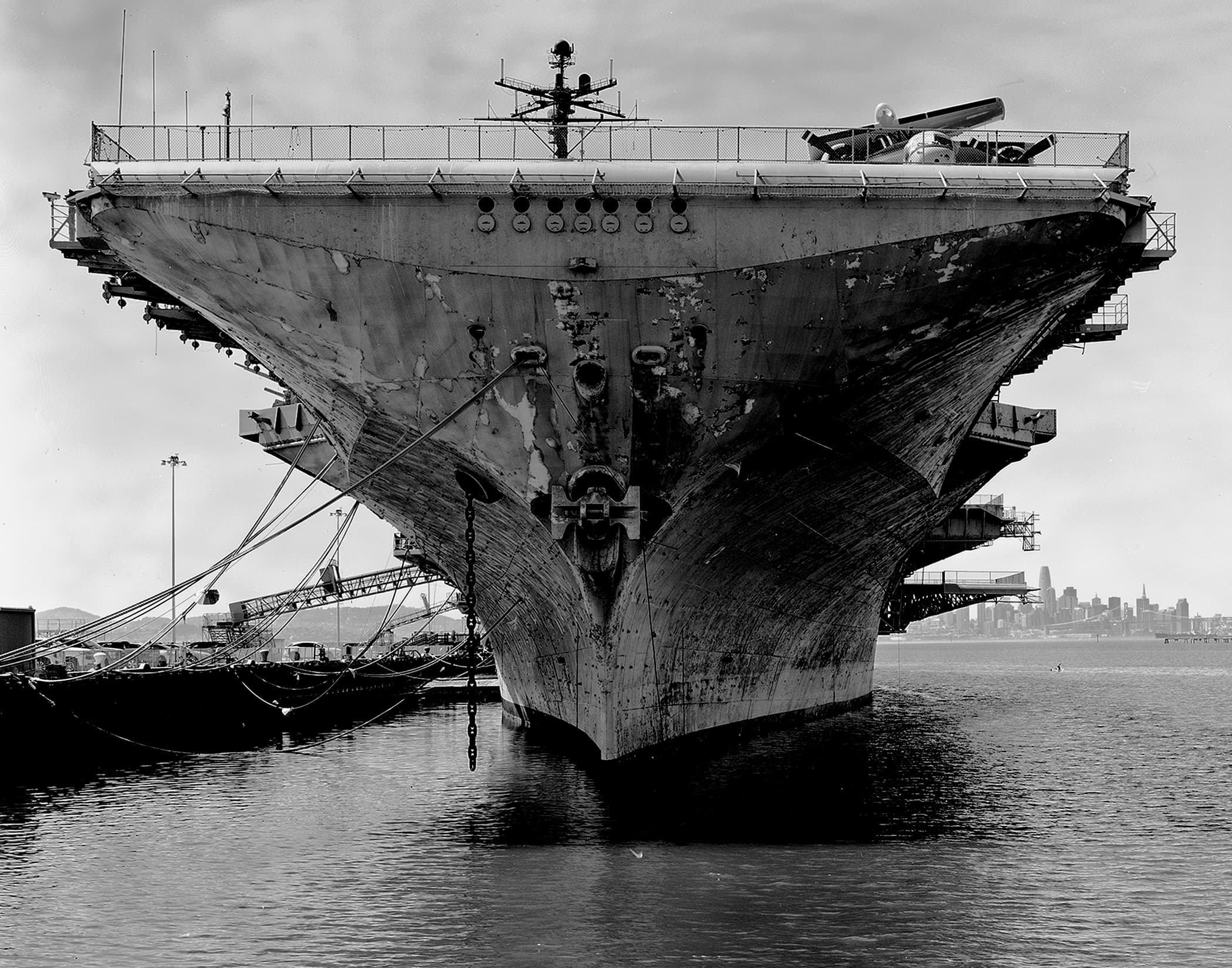 Black-and-white view of a weathered ship bow, anchor chain, and harbor water