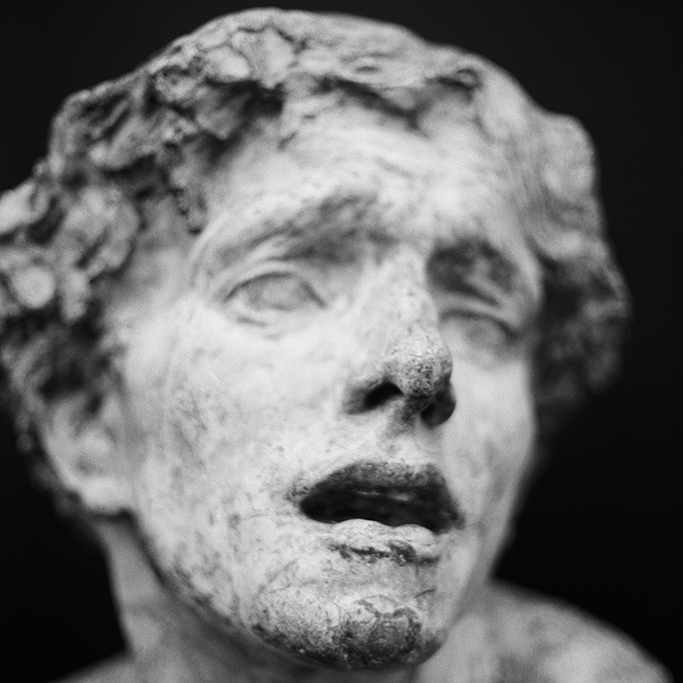 Close-up of weathered classical marble sculpture face with curly hair against dark background