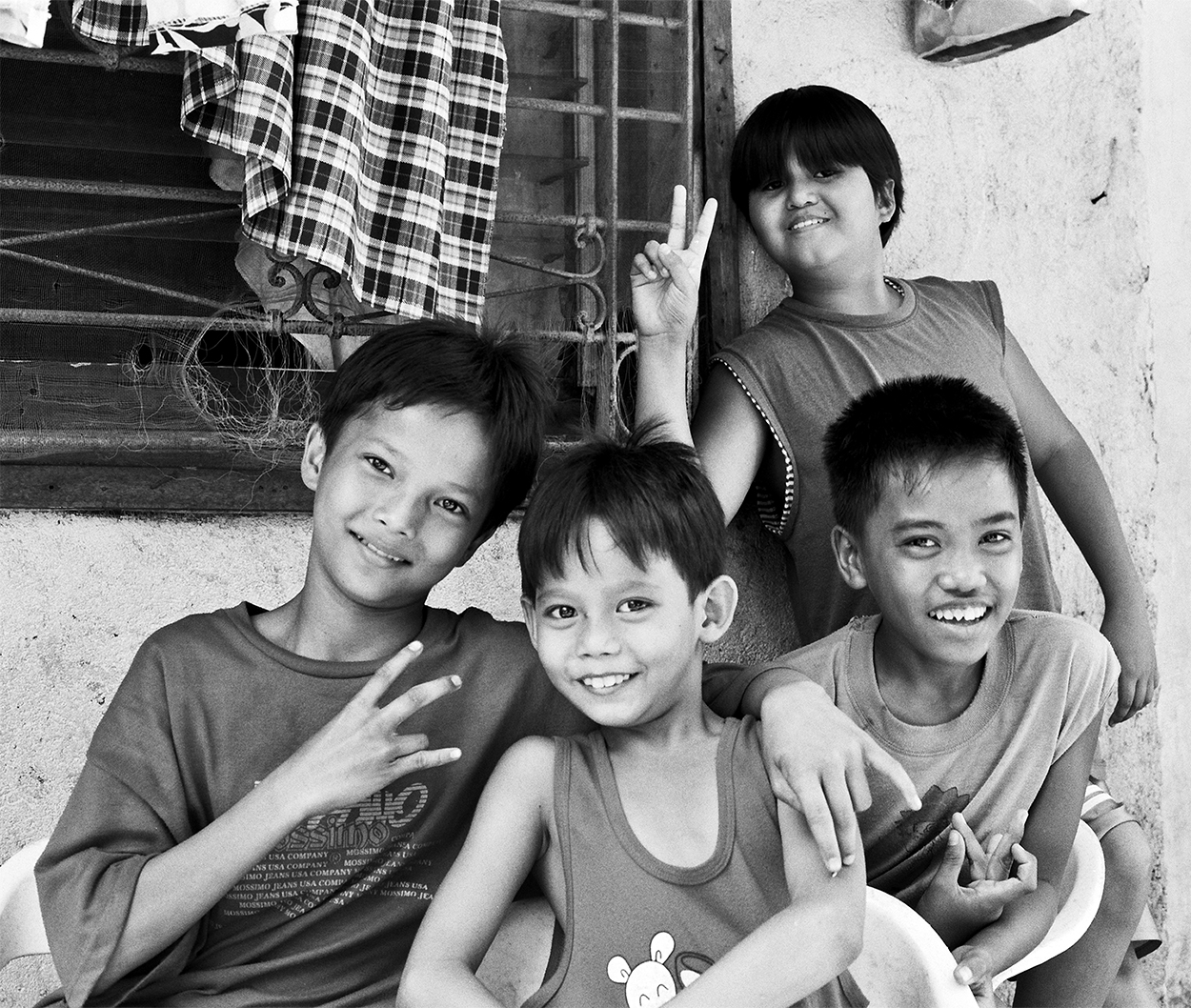 Four Filipino children smiling with peace signs in residential neighborhood