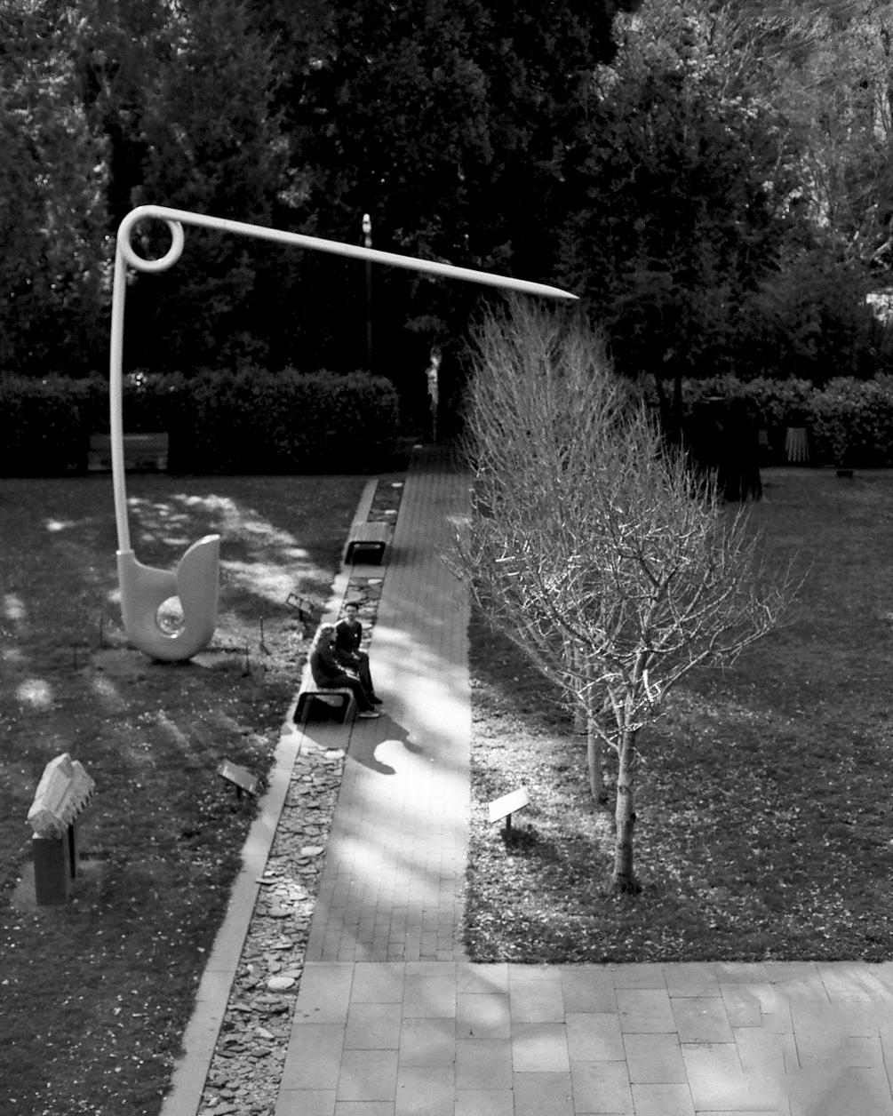 Modern sculptural white art installation in San Francisco park with dappled sunlight and figure sitting beneath